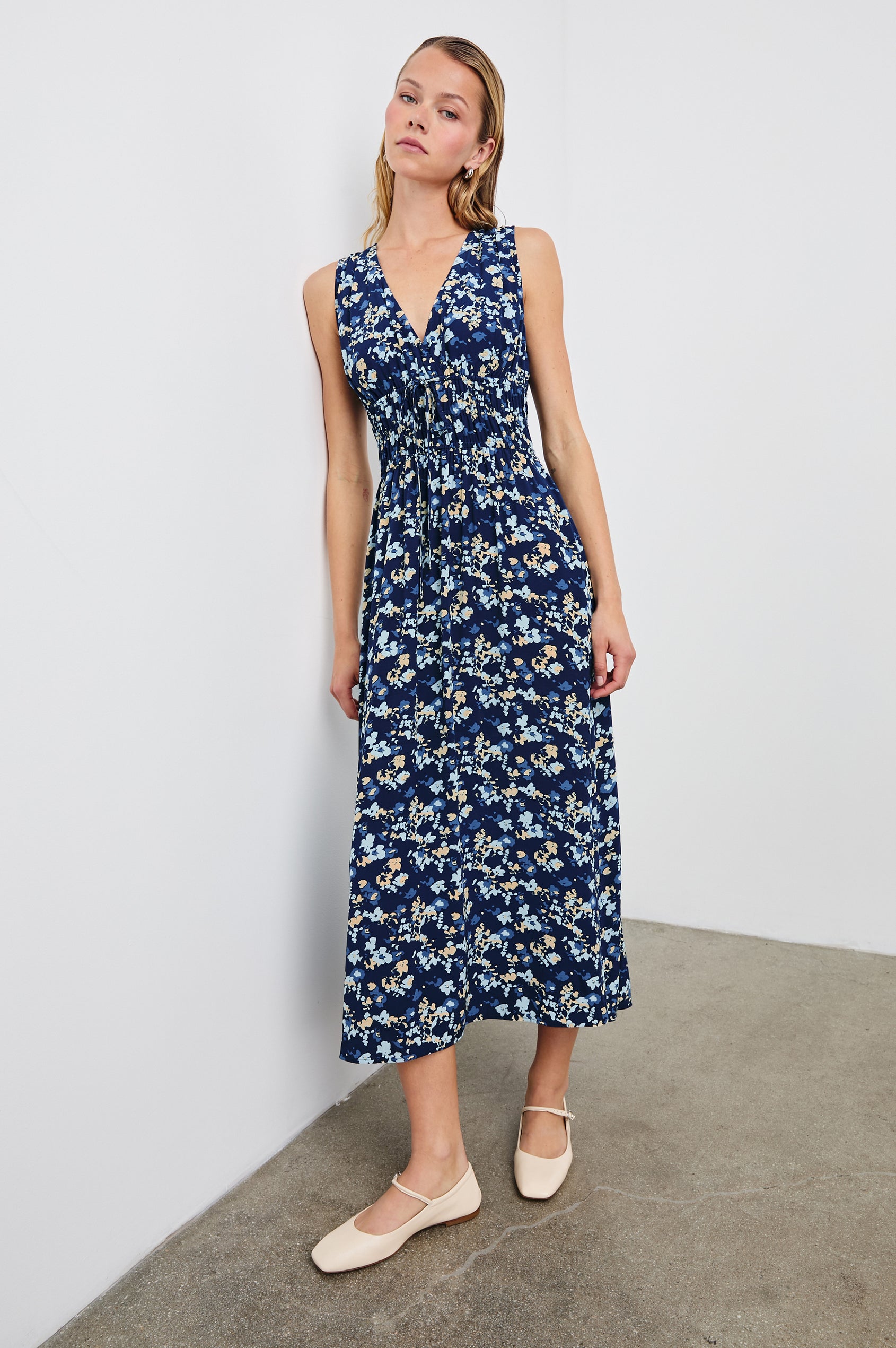 Lilith Sleeveless Midi Dress with Wide Shoulder Straps, a Deep V neck, a Cinched Waist with Drawstring, and a Back Neck Tie in Navy Flora Colorway, with flowers in creams and blues on Navy - Front Full Body View Featured on Model  