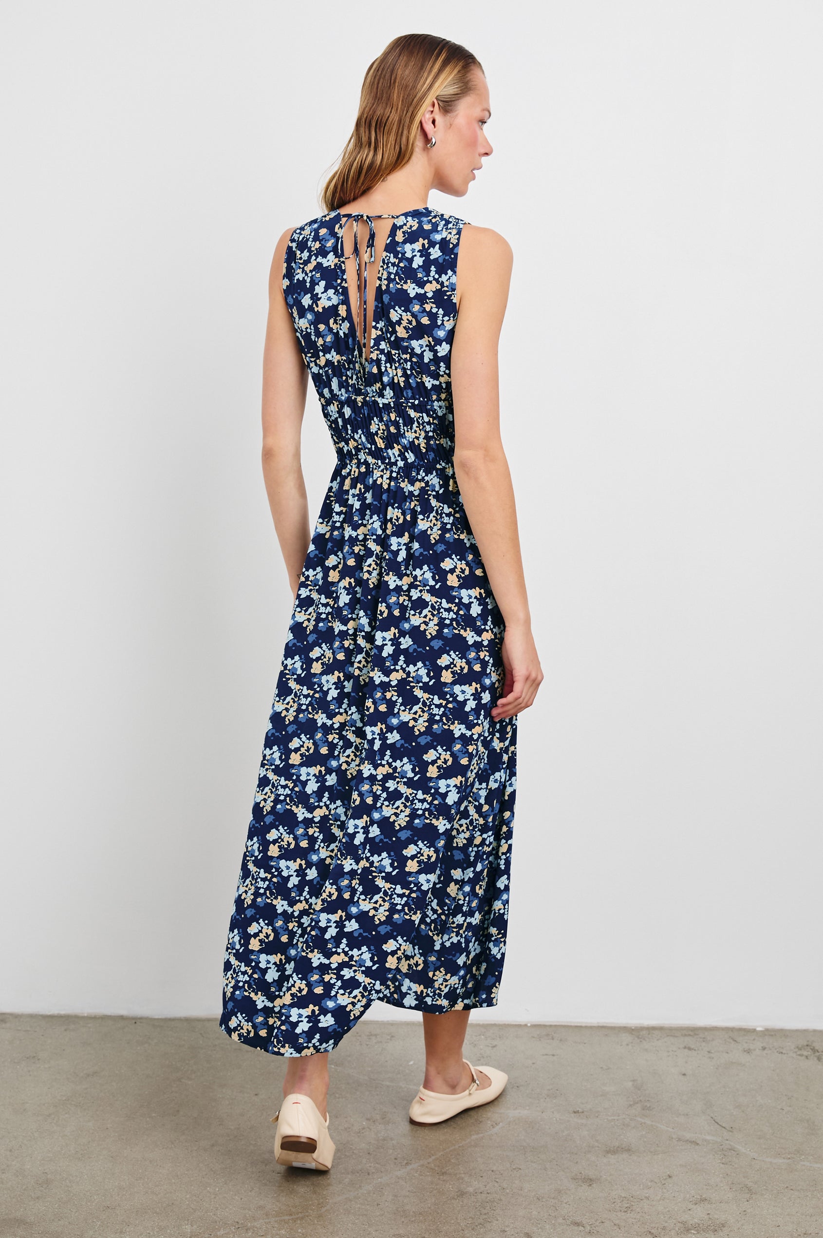Lilith Sleeveless Midi Dress with Wide Shoulder Straps, a Deep V neck, a Cinched Waist with Drawstring, and a Back Neck Tie in Navy Flora Colorway, with flowers in creams and blues on Navy - Back Full Body View Featured on Model  