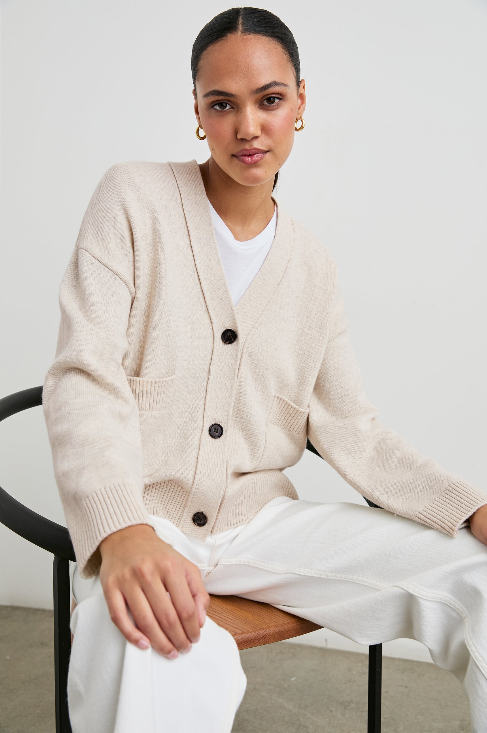 Lindi Long-Sleeve V Neck Cardigan with Three Button Closure, Two Front Patch Pockets and Ribbed Trim in Oatmeal Colorway - Front Full Body View Featured on Seated Model