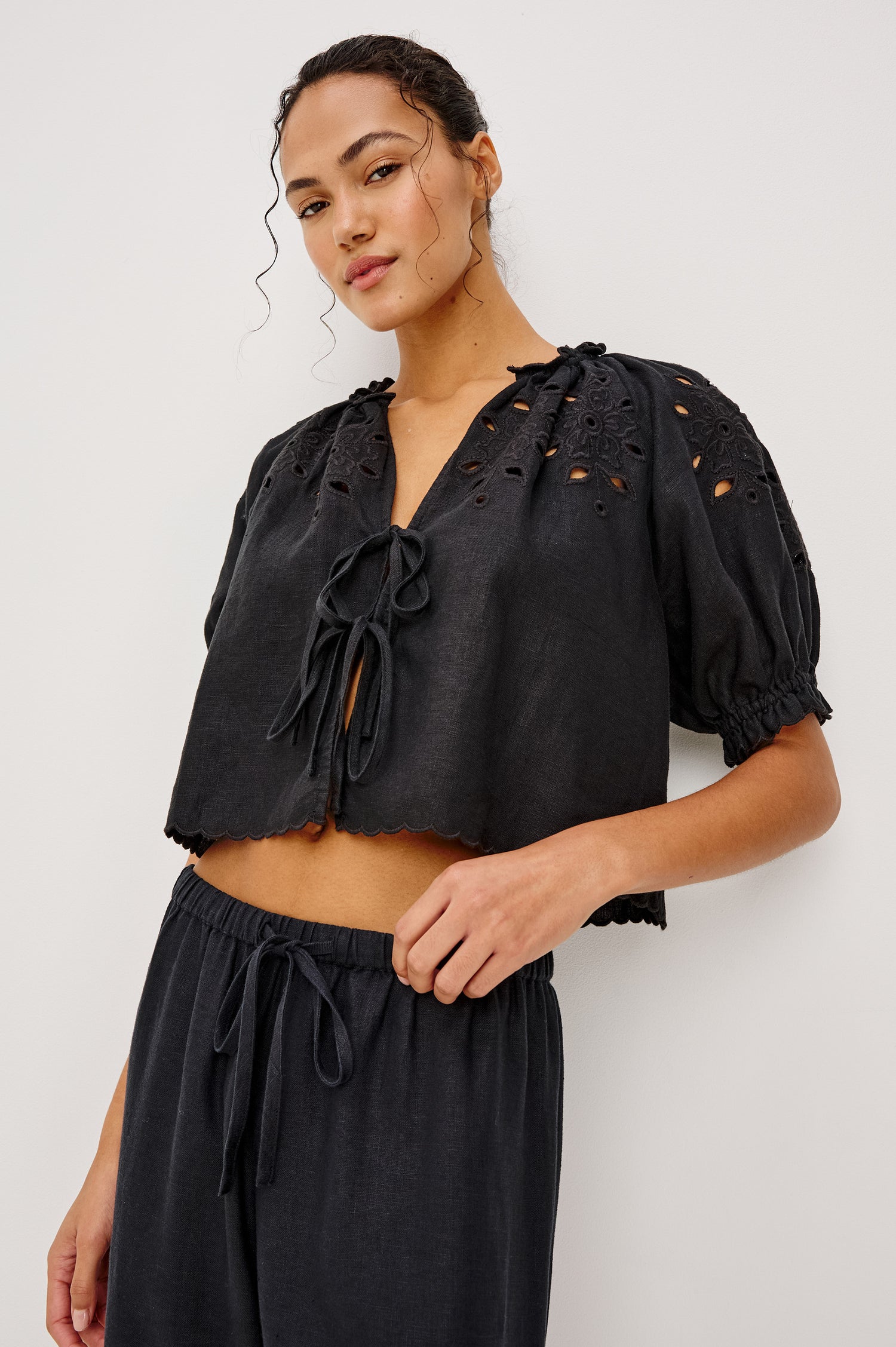 Lizbeth Milkmaid Top in Linen With Floral Eyelet Cutwork Plunging Tie-Front V-Neckline Front Ties Relaxed FIt Short Puff Sleeves in Black Ctolorway - Upper Body Front View Featured on Model