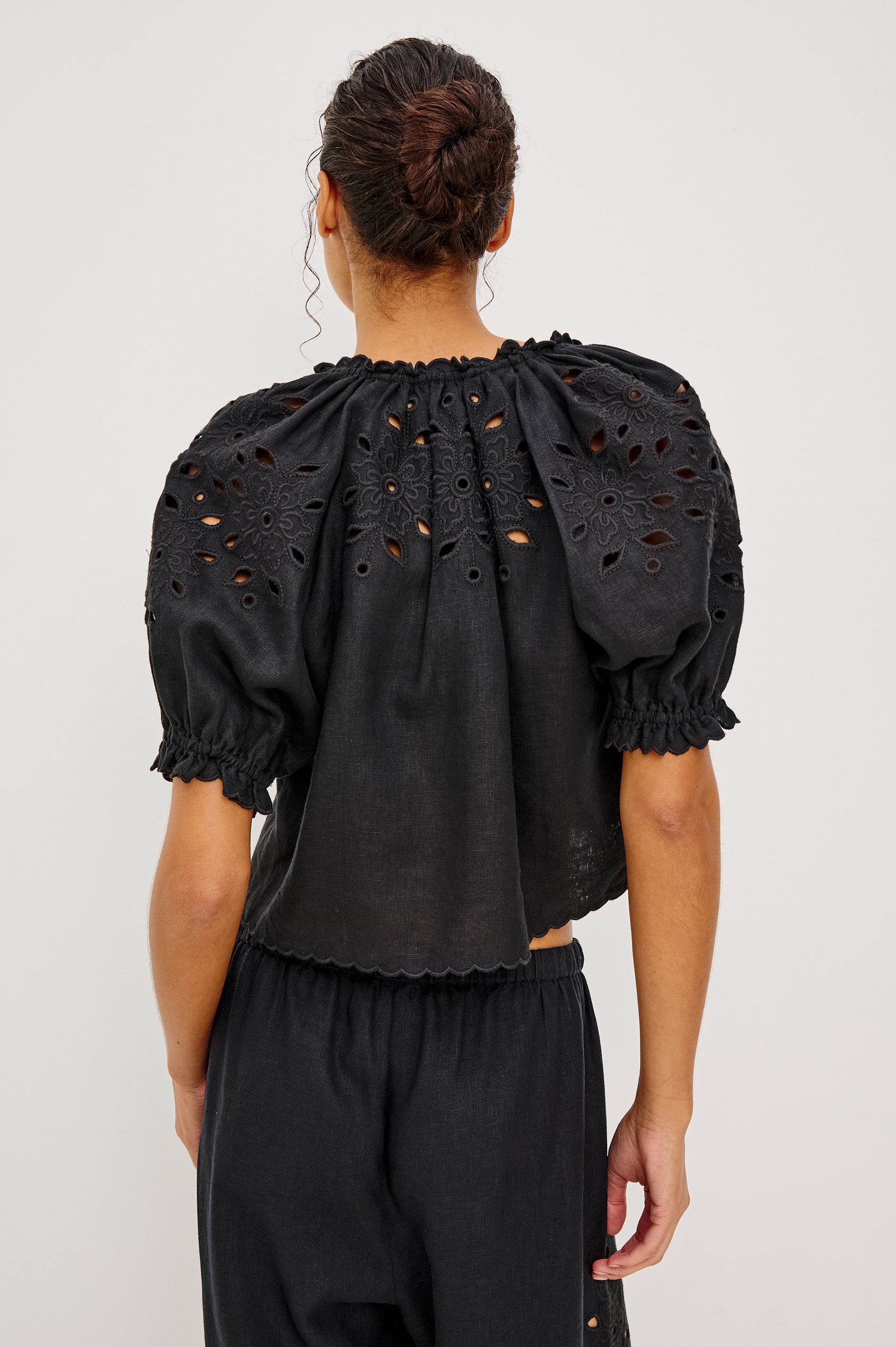 Lizbeth Milkmaid Top in Linen With Floral Eyelet Cutwork Plunging Tie-Front V-Neckline Front Ties Relaxed FIt Short Puff Sleeves in Black Ctolorway - Upper Body Back View Featured on Model