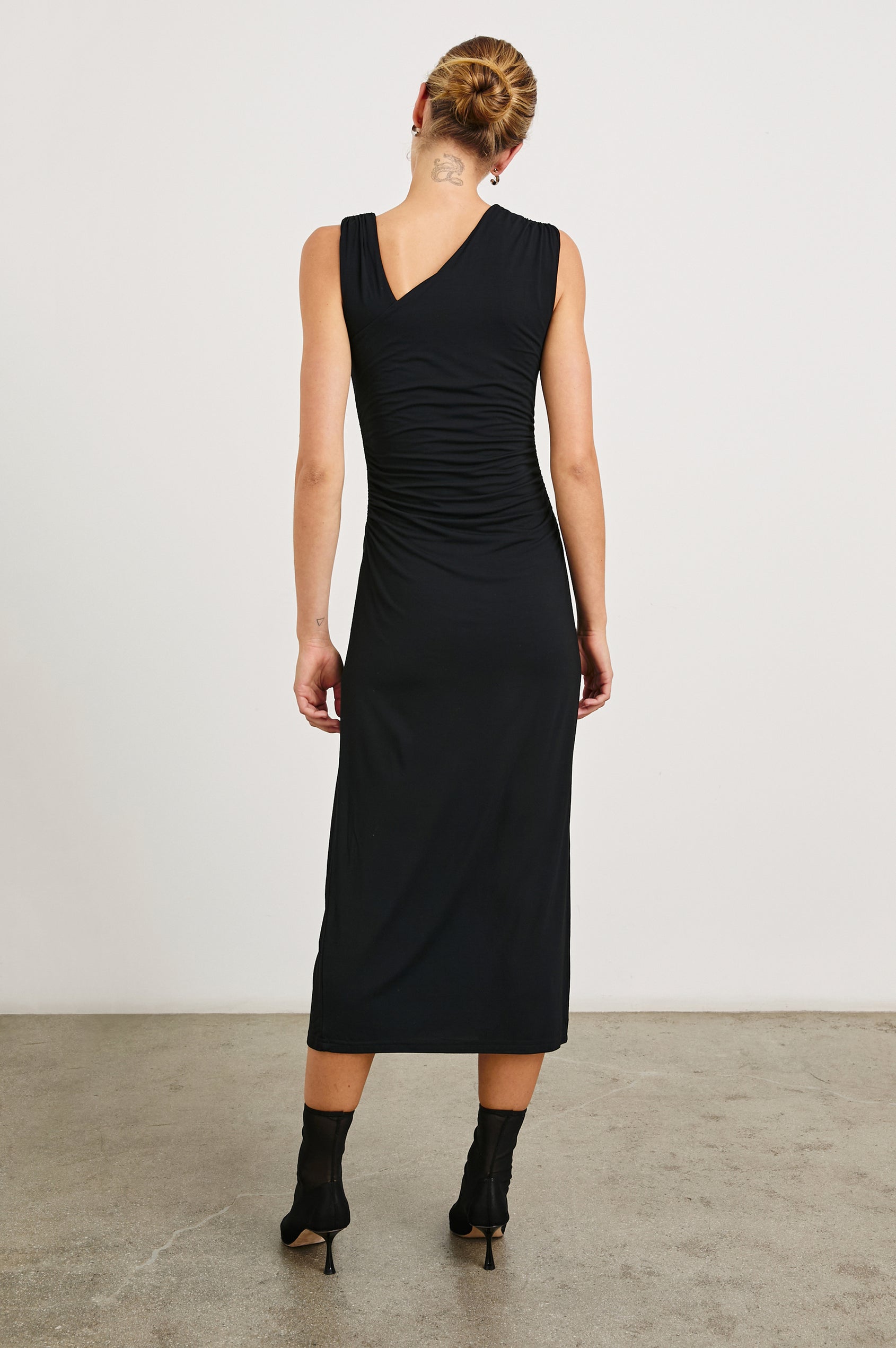 Lola Sleeveless Midi Dress with Ruching Along Both Bodice Sides, a Mid-Thigh Side Slit and an Asymmetrical Neckline in Black Onyx Colorway - Back Full Body View Featured on Model