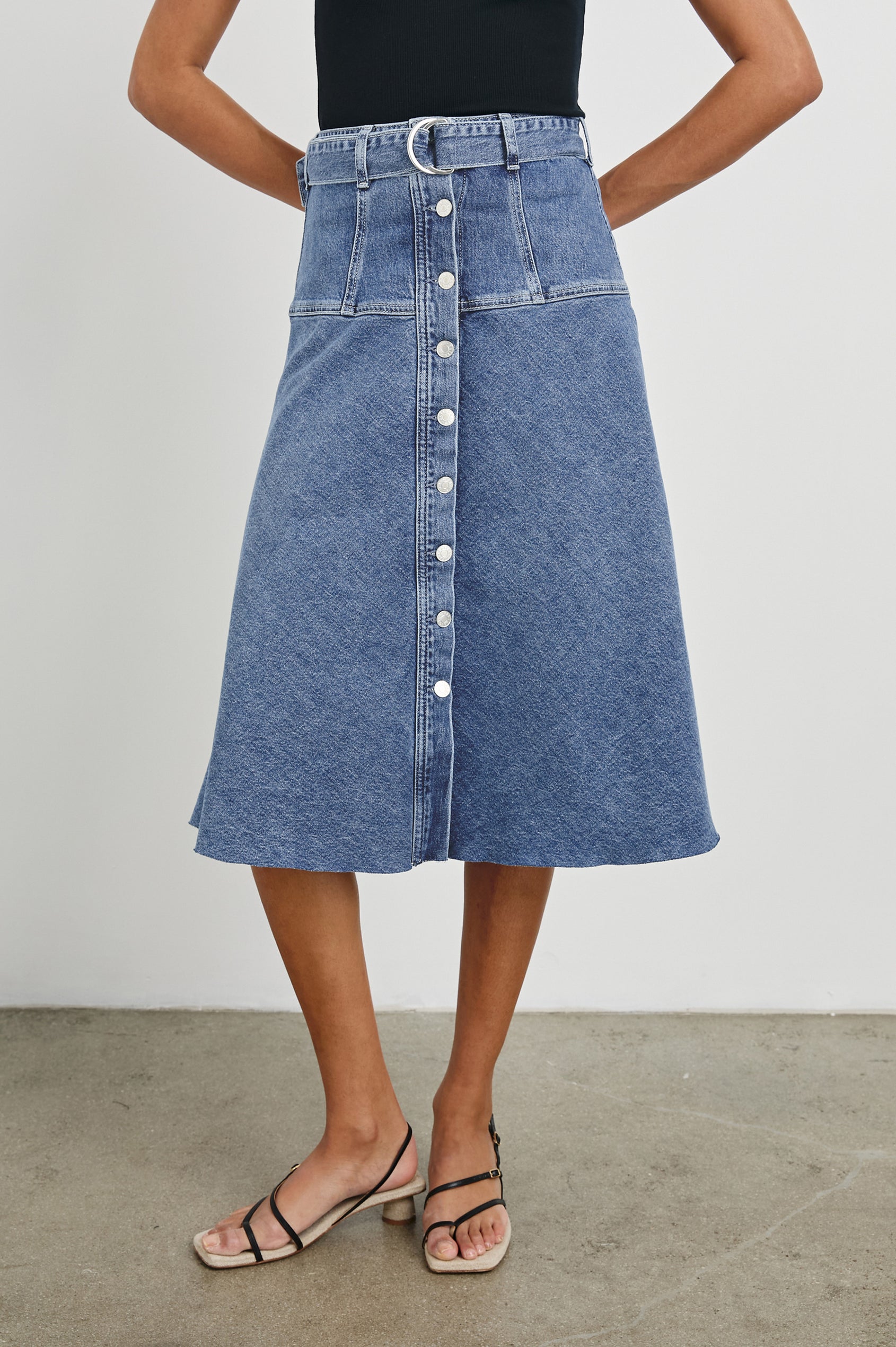 Loma Below-Knee A-Line Denim Skirt with an Exposed Button Front Opening, Adjustable Self Belt with D-Ring Closure and a Raw Hem in Pacific Coast Colorway. Front View Shown on Model.
