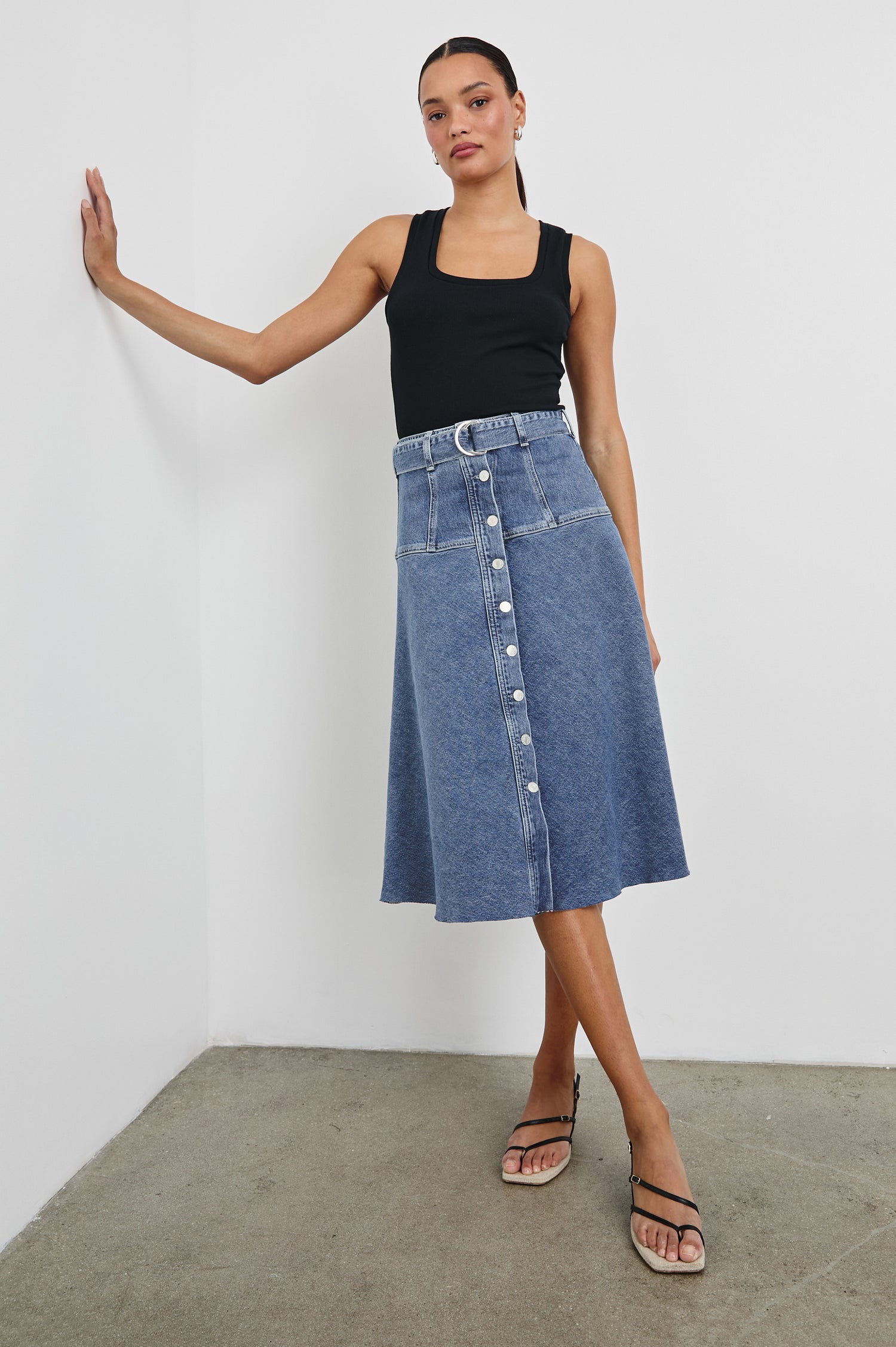 Loma Below-Knee A-Line Denim Skirt with an Exposed Button Front Opening, Adjustable Self Belt with D-Ring Closure and a Raw Hem in Pacific Coast Colorway. Full Body Front View Shown on Model.