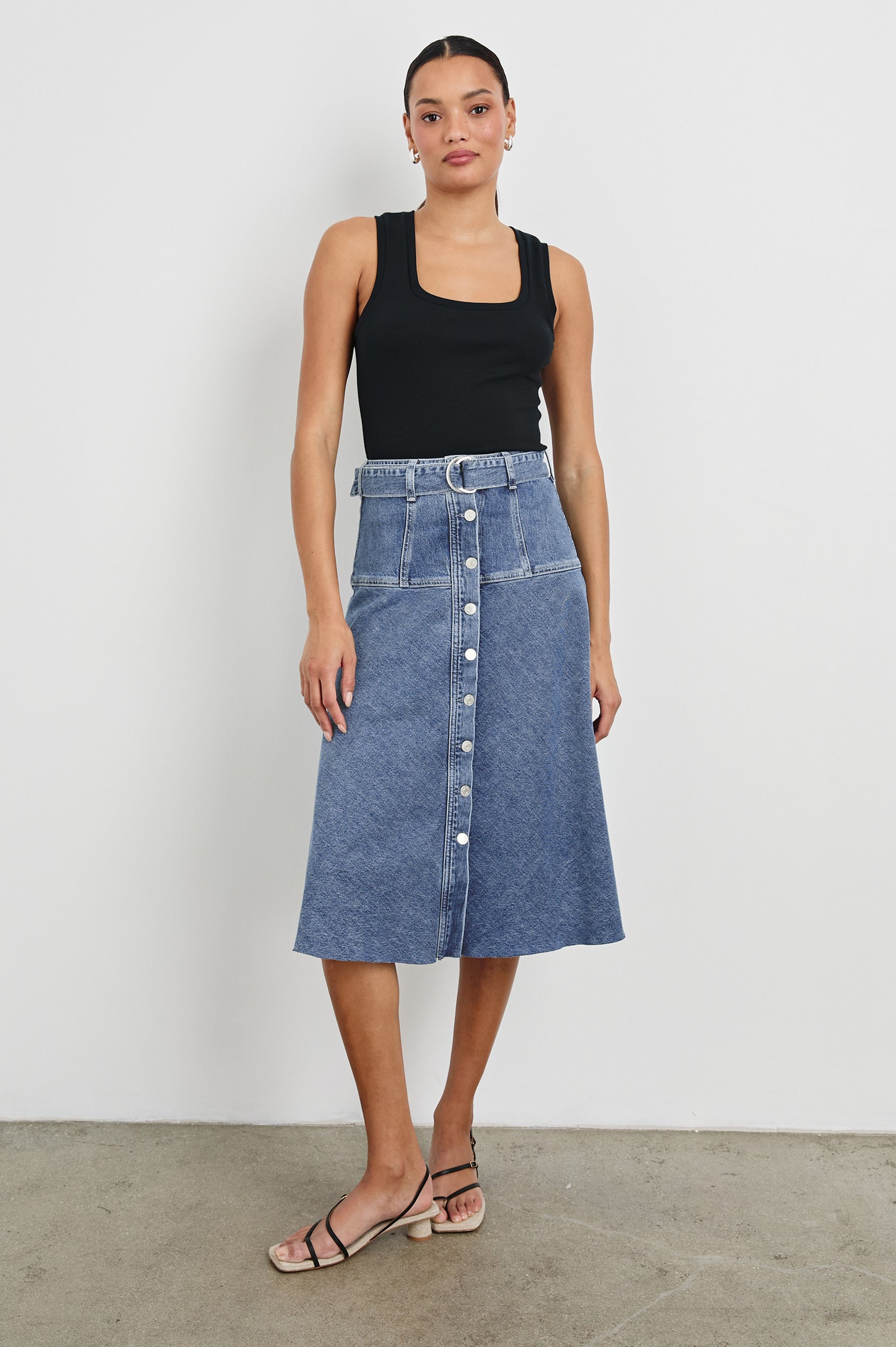 Loma Below-Knee A-Line Denim Skirt with an Exposed Button Front Opening, Adjustable Self Belt with D-Ring Closure and a Raw Hem in Pacific Coast Colorway. Full Body Front View Shown on Model.