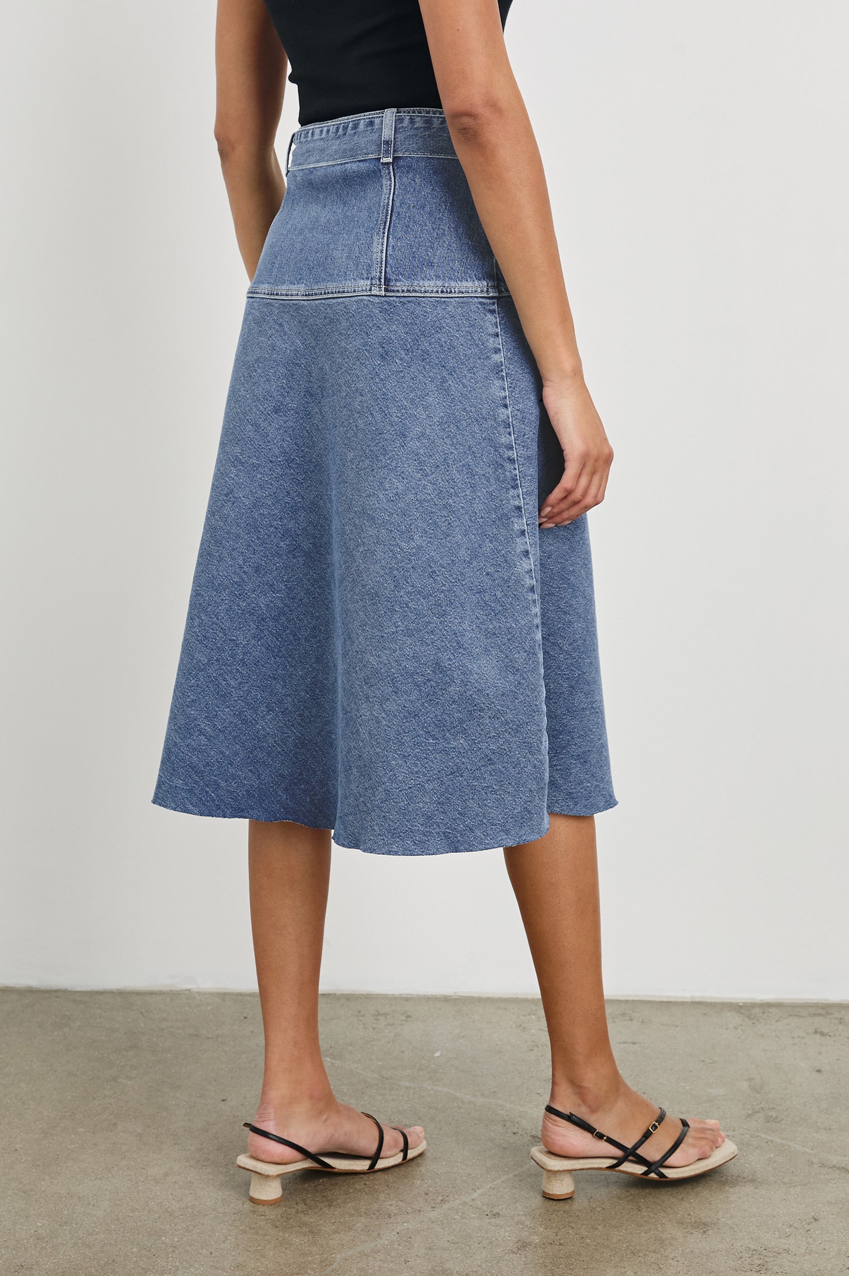 Loma Below-Knee A-Line Denim Skirt with an Exposed Button Front Opening, Adjustable Self Belt with D-Ring Closure and a Raw Hem in Pacific Coast Colorway. Back View Shown on Model.