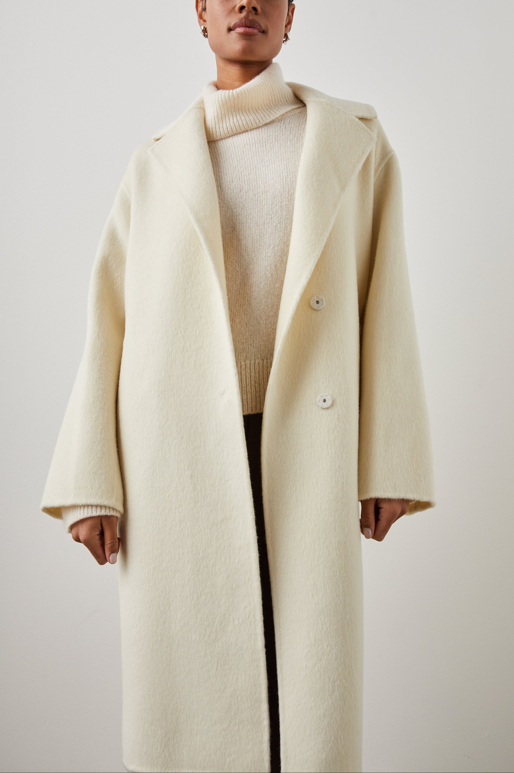Lore Knee-Length Coat with Two Button Closure, Notched Lapels and Two Front Pockets in Ivory Colorway - Front Full Body View Featured on Model