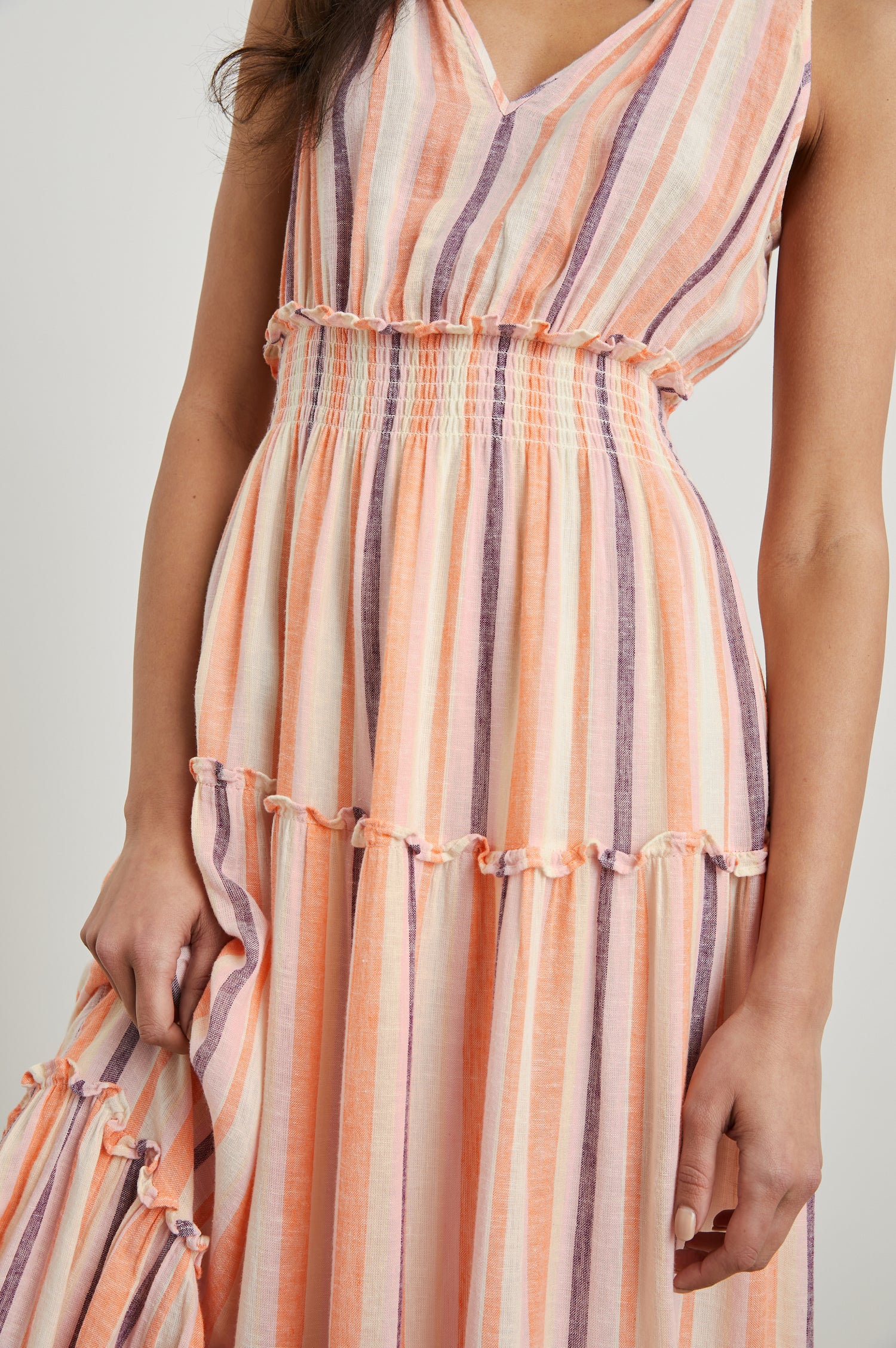Loulou Sleeveless Midi Dress with a V Neck, Shirred Collar, Smocked Waist and Tiered Skirt in Papaya Stripe Colorway, purple, oranges and cream vertical Stripes - Front View Featured on Model