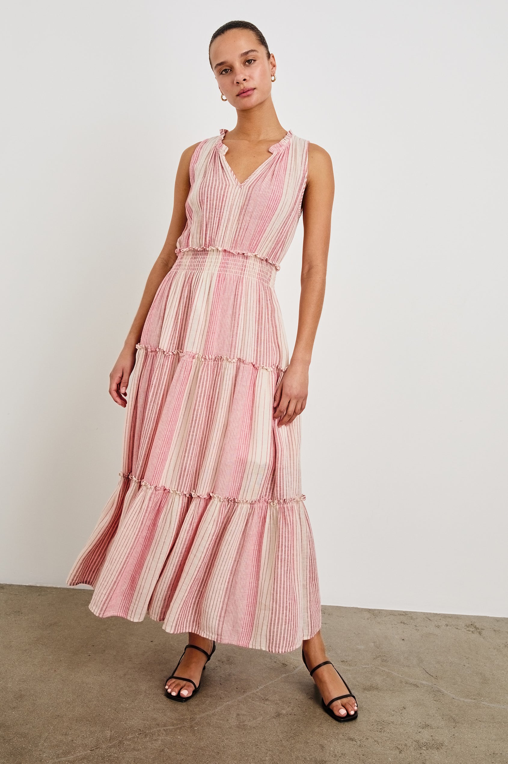 Front view of female model wearing our sleeveless, Loulou Maxi Dress in color Salerno Stripe, a pink and white boho stripe. Dress features smocked waist, v-neck, and tiered maxi skirt. 