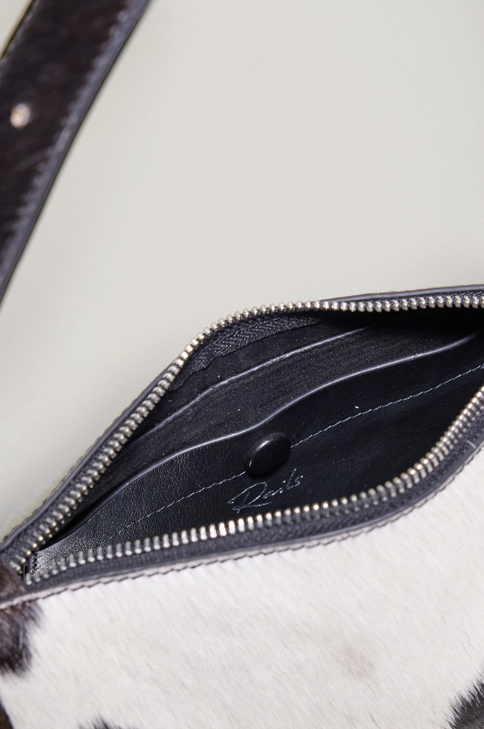 The Lucca is a long-hair cowhide shoulder bag with an adjustable strap and polished silver oval buckle. In Cowgirl Haircalf colorway. Close up view of interior featured.