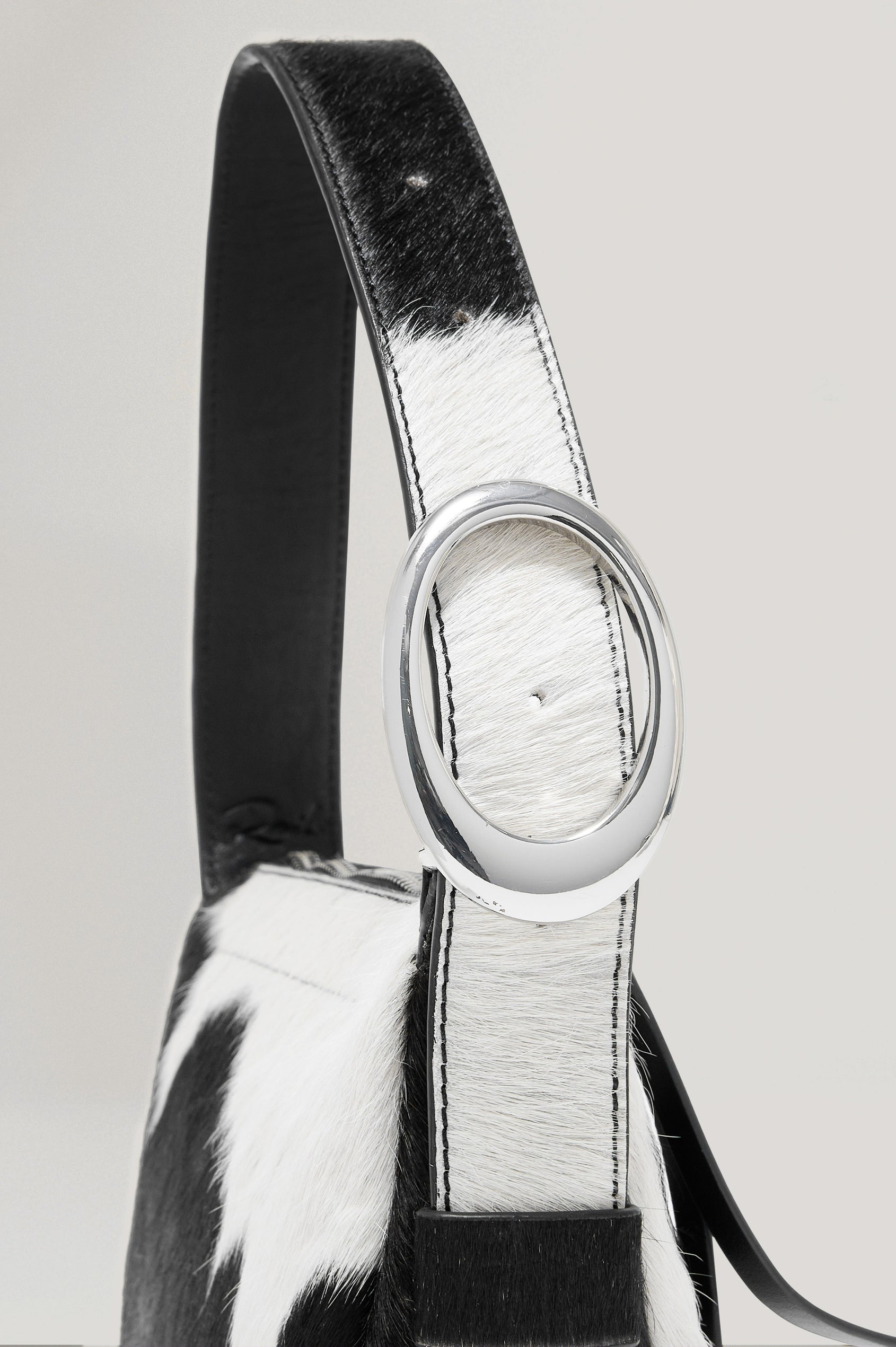 The Lucca is a long-hair cowhide shoulder bag with an adjustable strap and polished silver oval buckle. In Cowgirl Haircalf colorway. Close up view of strap featured.