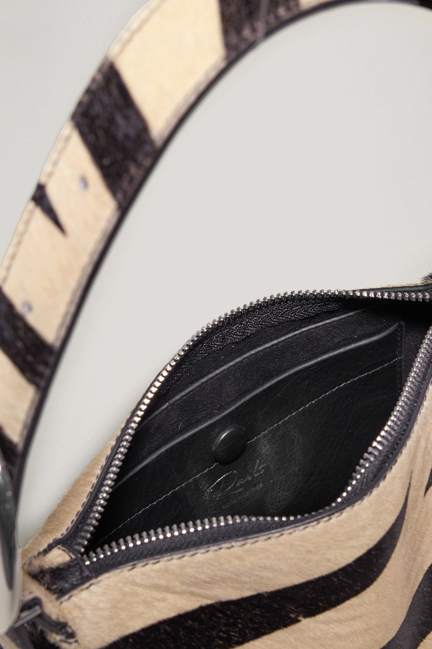 The Lucca is a long-hair cowhide shoulder bag with an adjustable strap and polished silver oval buckle. In Zebra Haircalf colorway. Close up view of interior featured.
