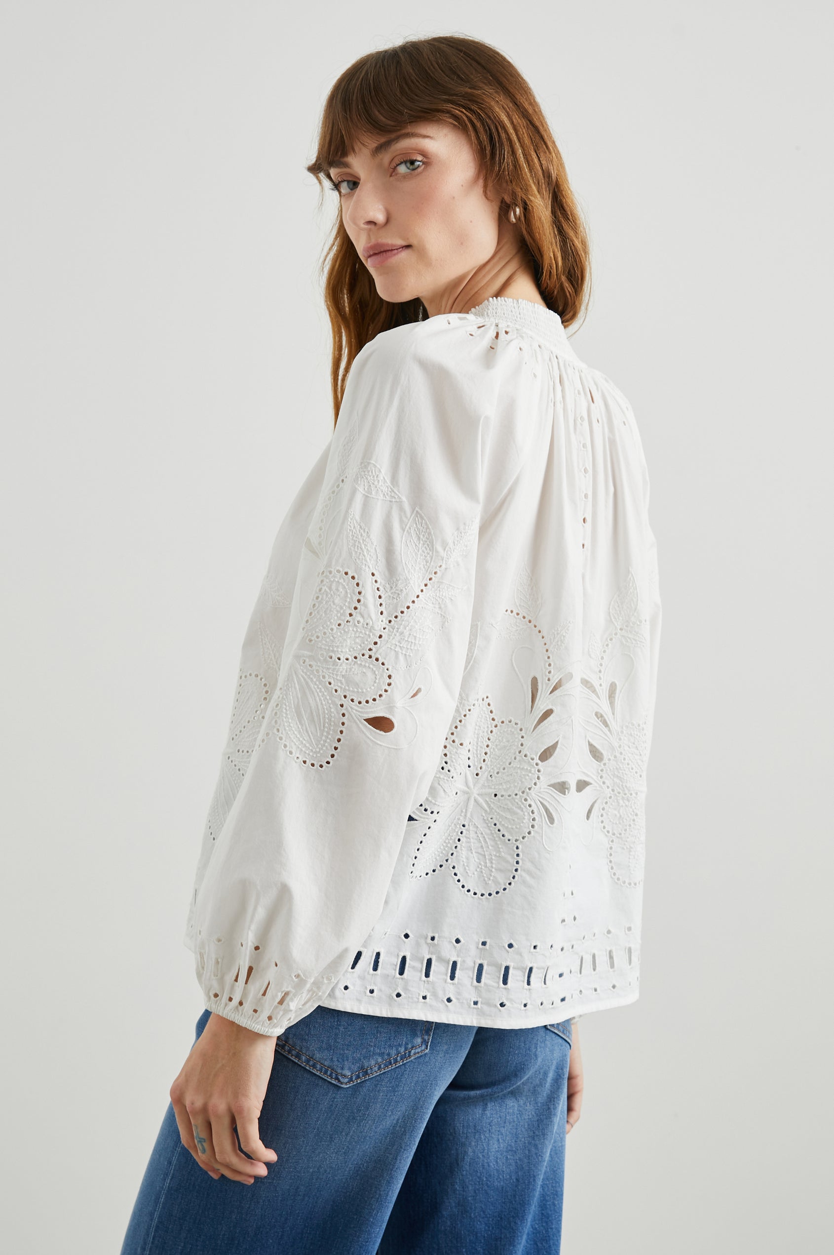 Lucinda Long-Sleeve Top with Billowy Sleeves, a V Neck with a Drawstring Collar, and a Floral and Geometric Eyelet Design in White Colorway - Side View Featured on Model  