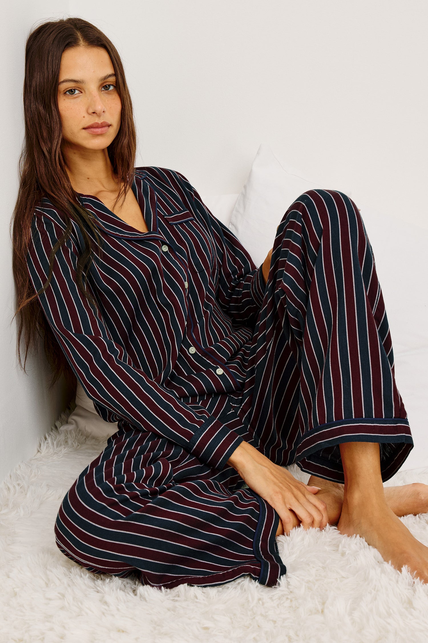 Luna Pajama Set in Signature Rayon With Button-Up Collared Shirt With Front Buttons, Long Sleeves, Chest Patch Pocket and Matching Pant With Side Pockets and Drawstring Waist Ties in Navy Oxblood Stripe Colorway - Full Body Front View Featured on Model Sitting