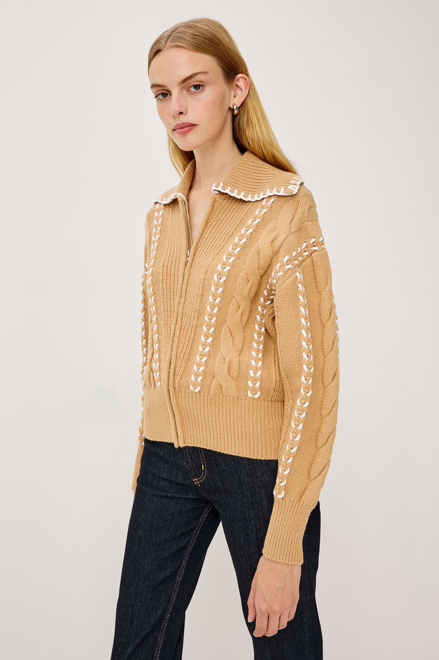 Lune Sweater in Cable Knit With Contrast Blanket Stitch Detailing, Stand Collar, Front Zipper, and Long Sleeves in Camel Ivory Blanket Stitch Colorway - Upper Body Front View Featured on Model