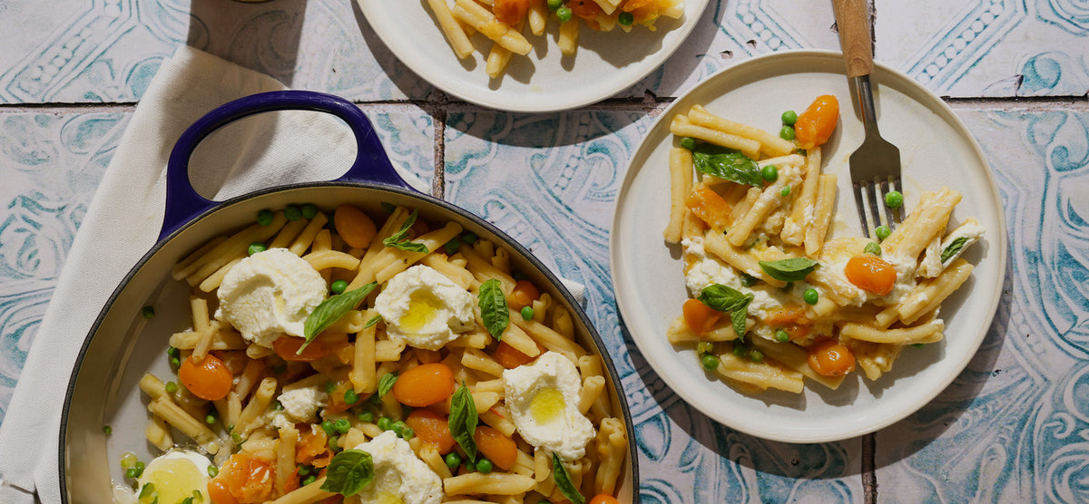 Pasta dish with eggs and vegetables on a plate and in a pan, served on a tiled table.