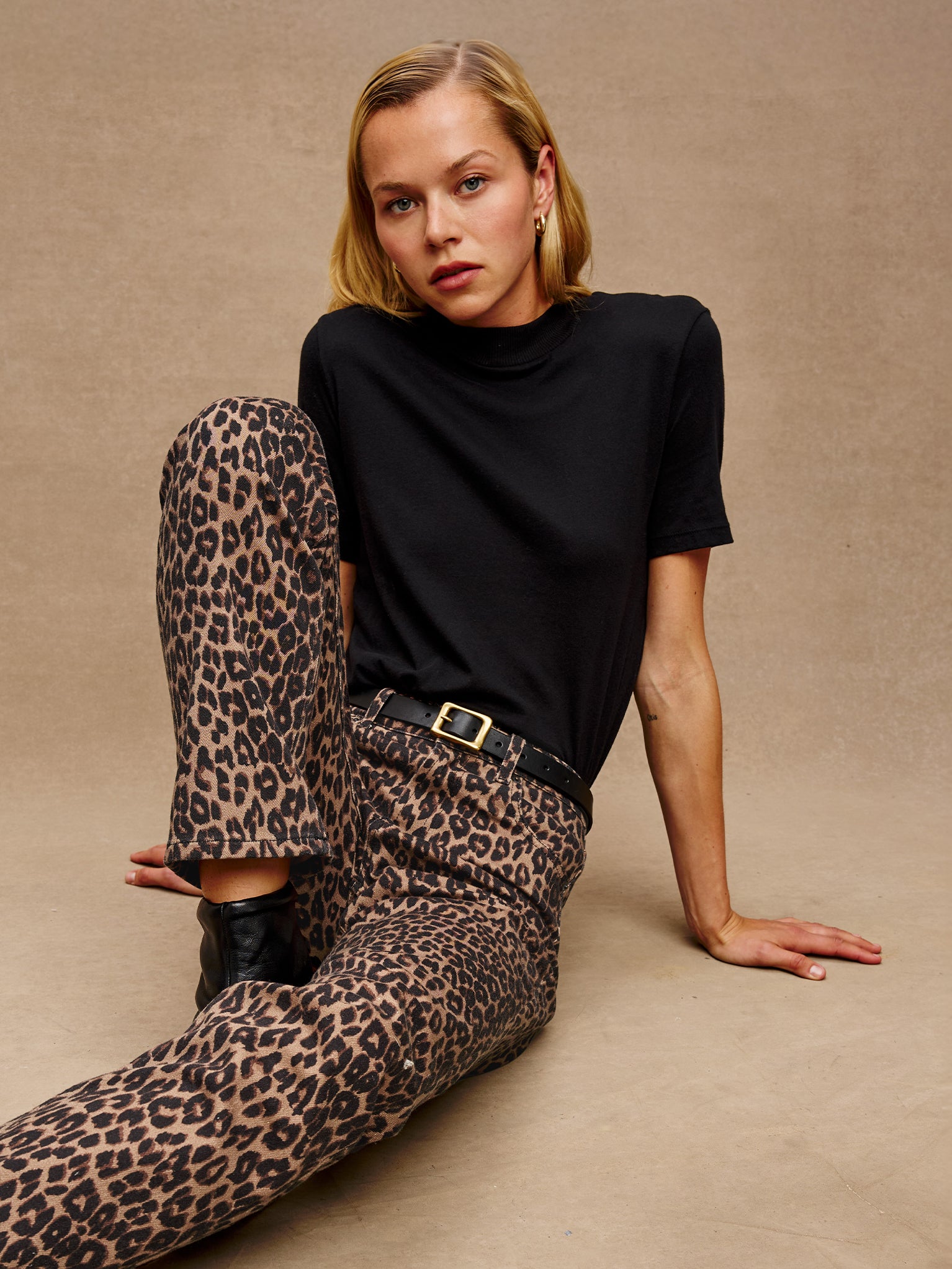 Woman wearing a black top and leopard print pants sitting on a beige background