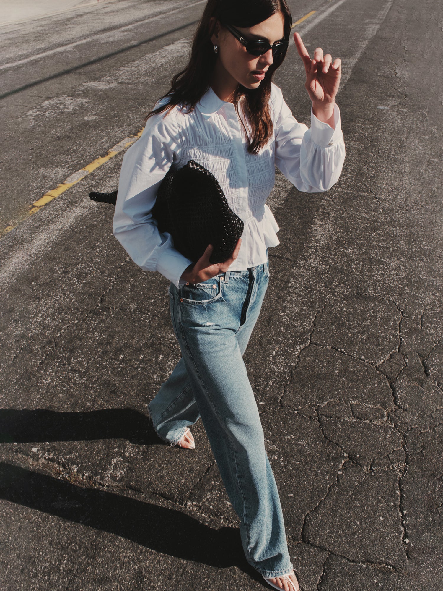 Woman in a white shirt and blue jeans holding a black clutch against a neutral background