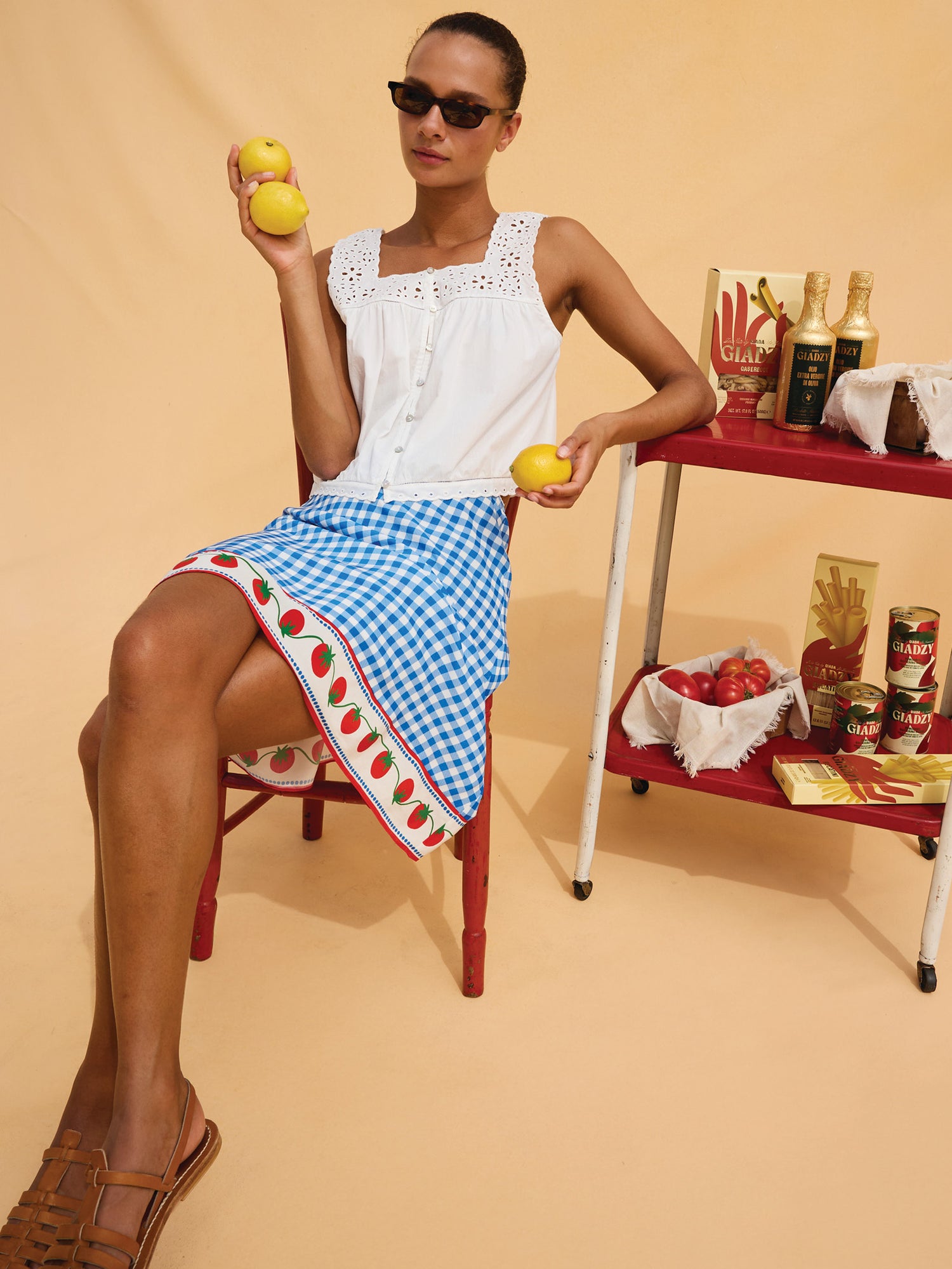 Woman in a white top and blue checkered skirt holding lemons against a beige background