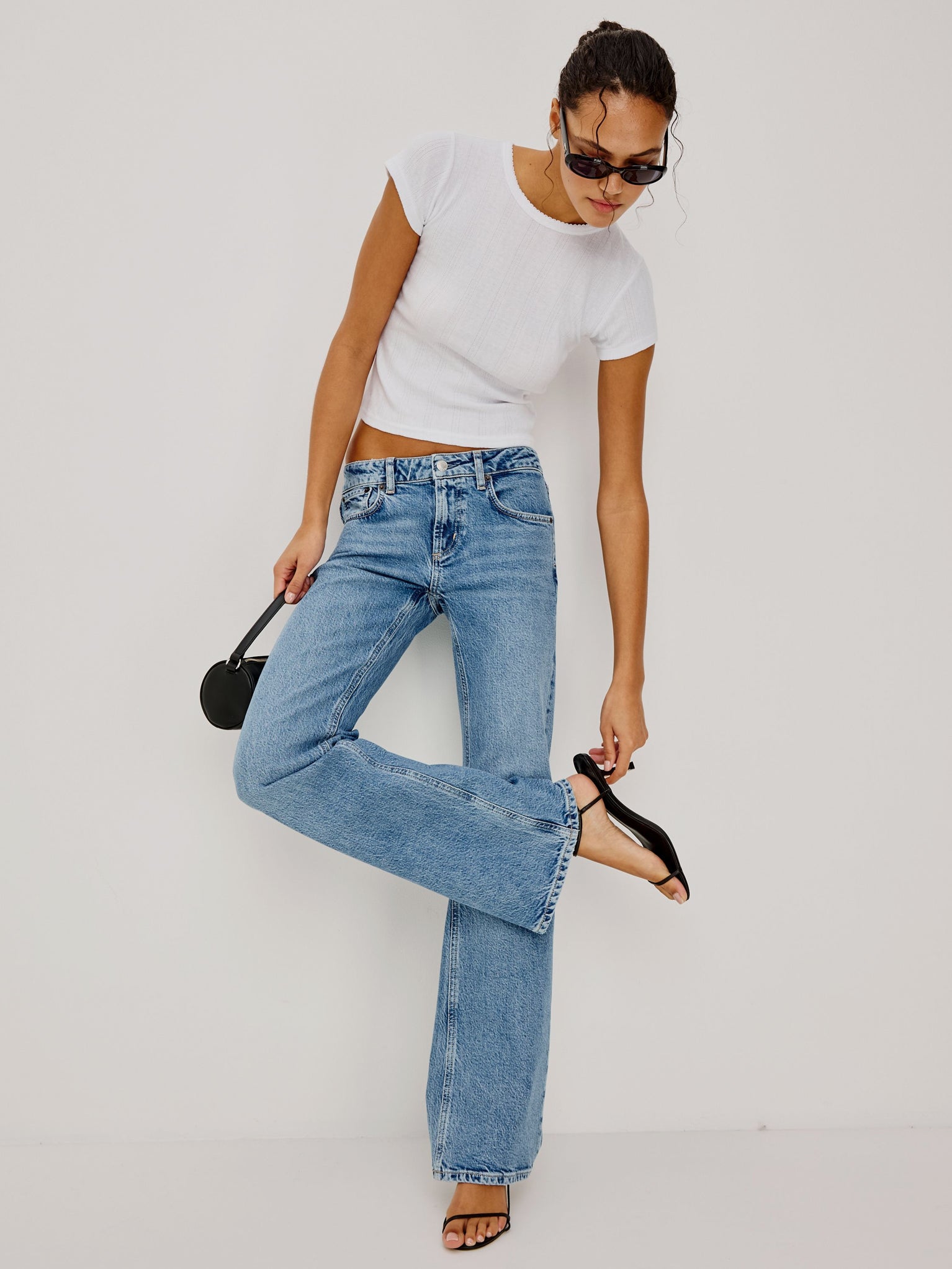 Woman wearing light blue jeans and a white top, posing against a plain background.