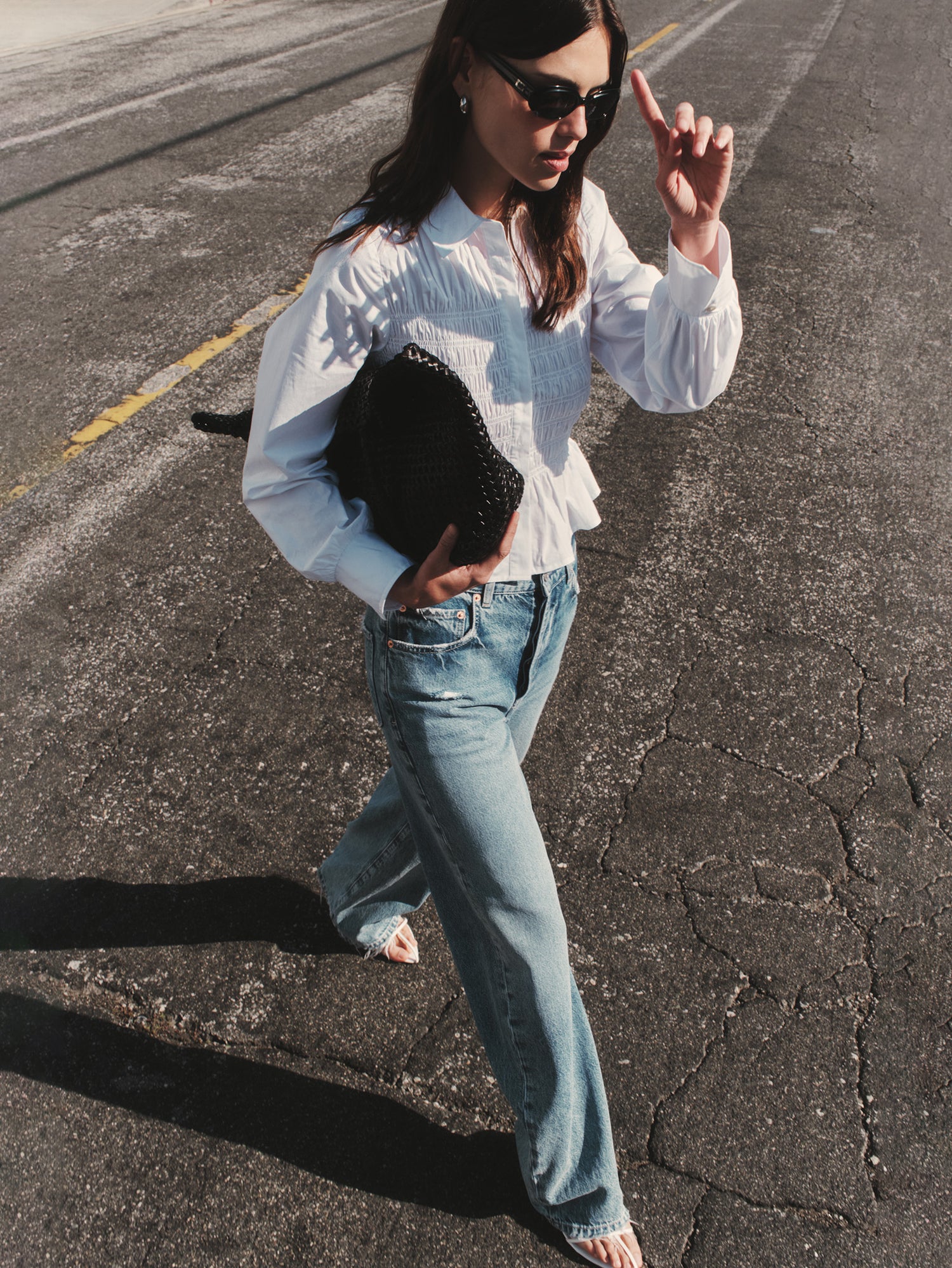 Woman wearing a white blouse and blue jeans while posing in the street