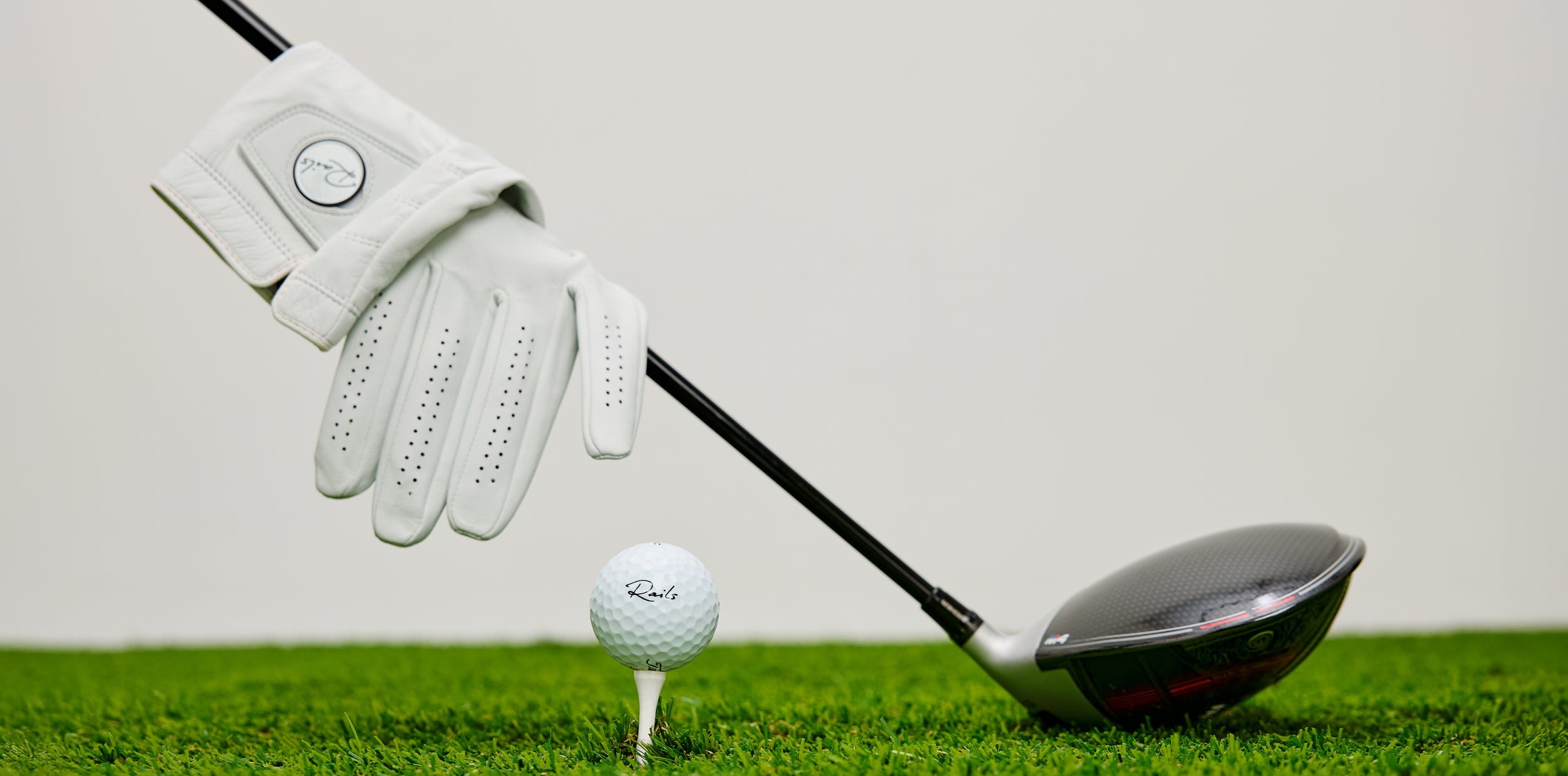 Golf club, golf ball, and glove on a grassy surface with a white background