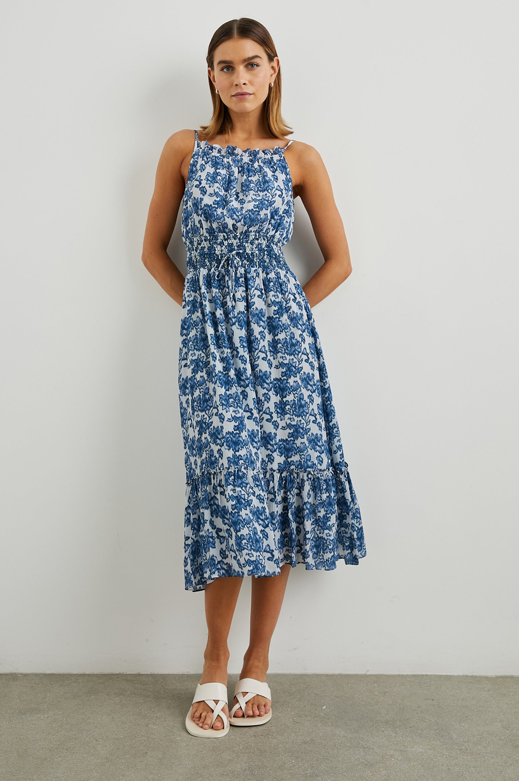 Magdalene Sleeveless Midi Dress with Spaghetti Straps, a Button Keyhole at the Back, a Shirred Waist with a Drawstring, a Scoop Neckline with Ruffled Trim, and a Ruffled Hem in Chambray Floral Colorway, Blue Flowers on White - Front Full Body View Featured on Model  