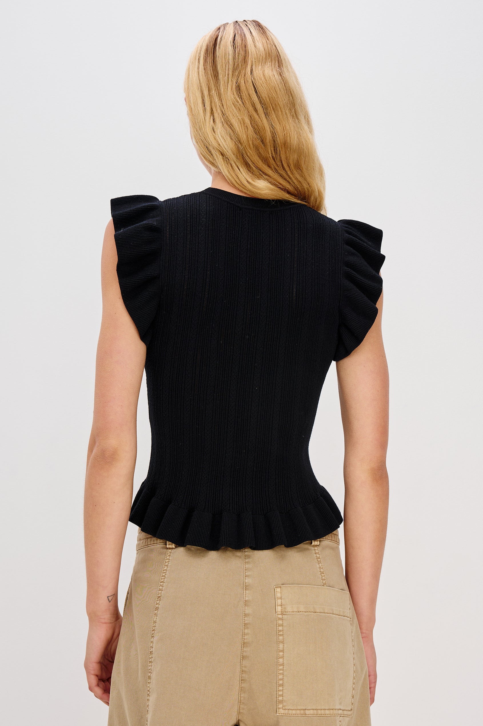 Marci is a short-sleeve fine-gauge knit sweater top. The fitted silhouette is accented with flutter sleeves and a ruffled hem in Black Colorway - Back View Featured on Model