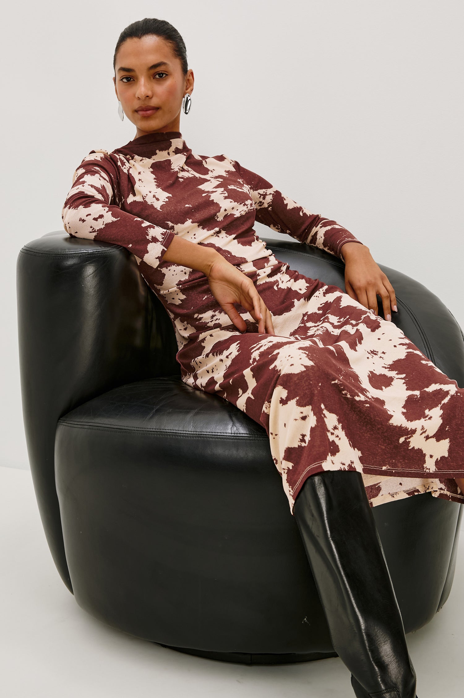 Margaret Long-Sleeve Midi Dress with a Mock Neck and Shirring along the Left Side in Cowgirl Colorway - Stylized Front View Featured on Model Sitting in Leather Chair