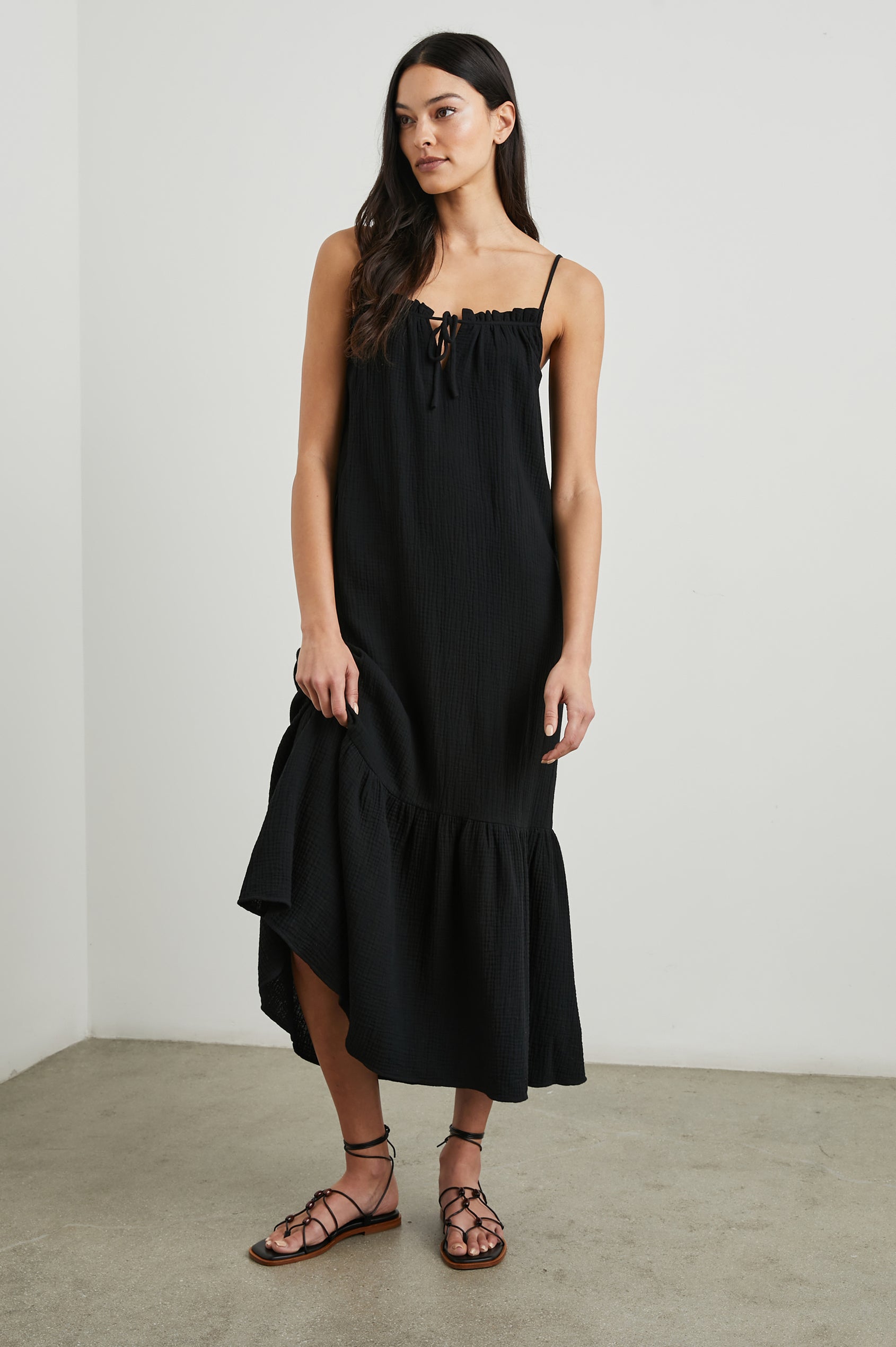 Marseille Midi Dress with Adjustable Spaghetti Straps, a Deep V Neck with a Tie, and a Lightly Ruffled Hem in Black Colorway - Front Full Body View Featured on Model