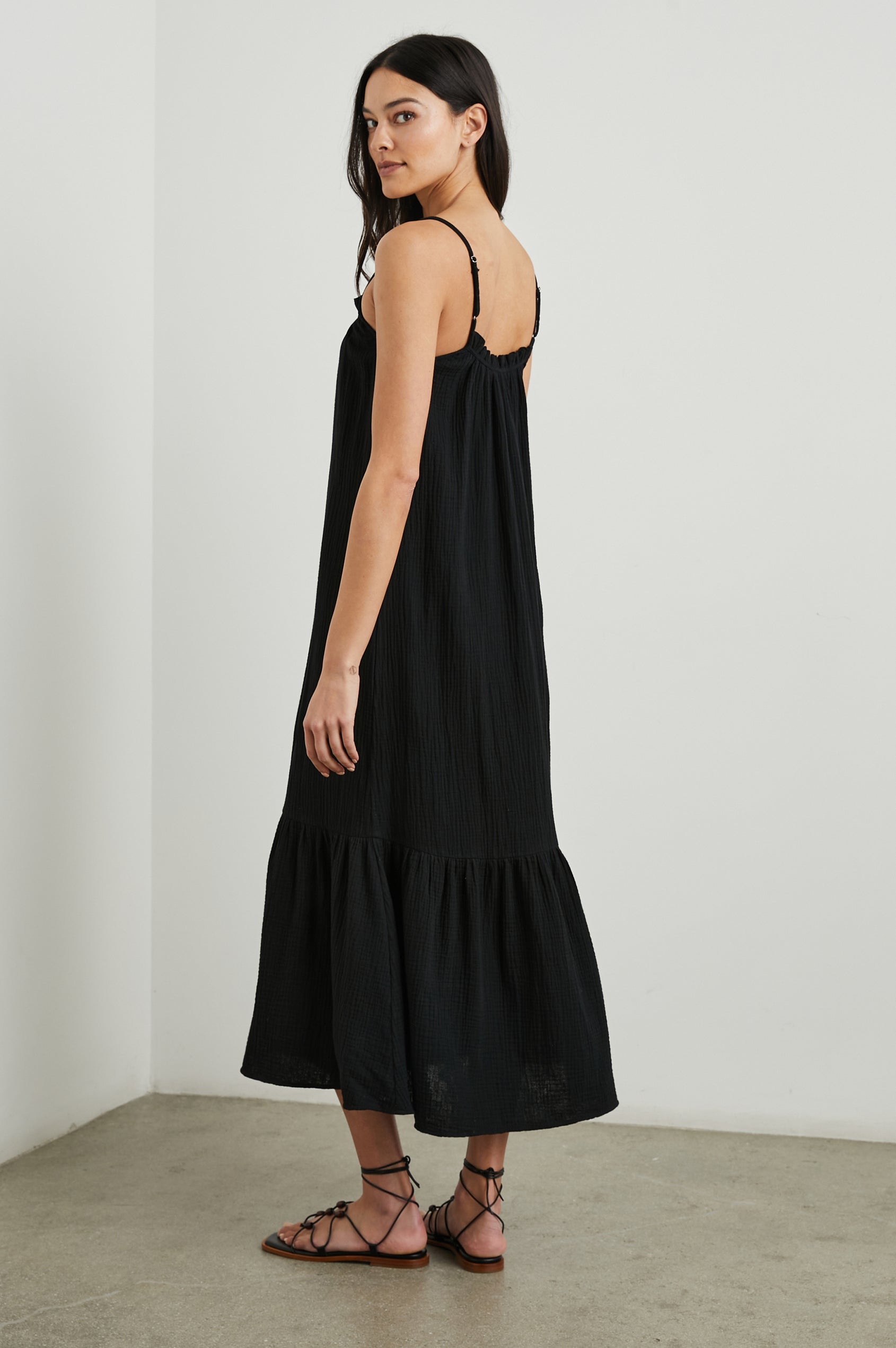 Marseille Midi Dress with Adjustable Spaghetti Straps, a Deep V Neck with a Tie, and a Lightly Ruffled Hem in Black Colorway - Side Full Body View Featured on Model