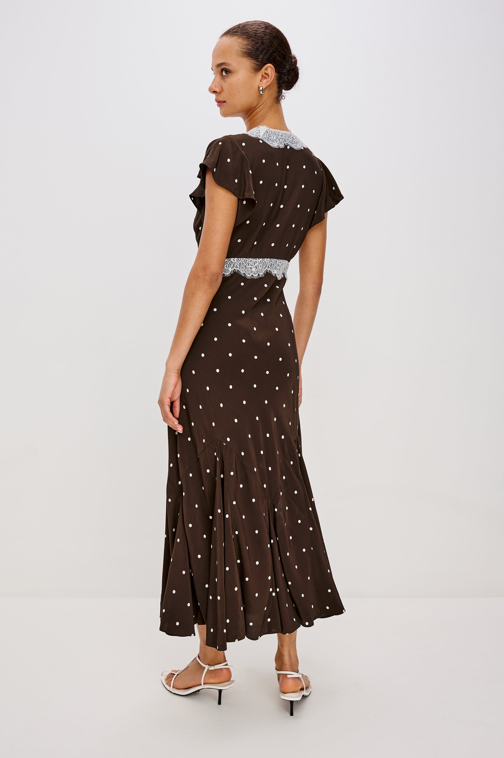 A flowing cocoa polka-dot maxi dress in crepe. The dress has a lace-trimmed V-neckline, ruffle cap sleeves, a hidden side zipper, and godet inserts that add movement to the skirt. Full Body Back View featured on Model.
