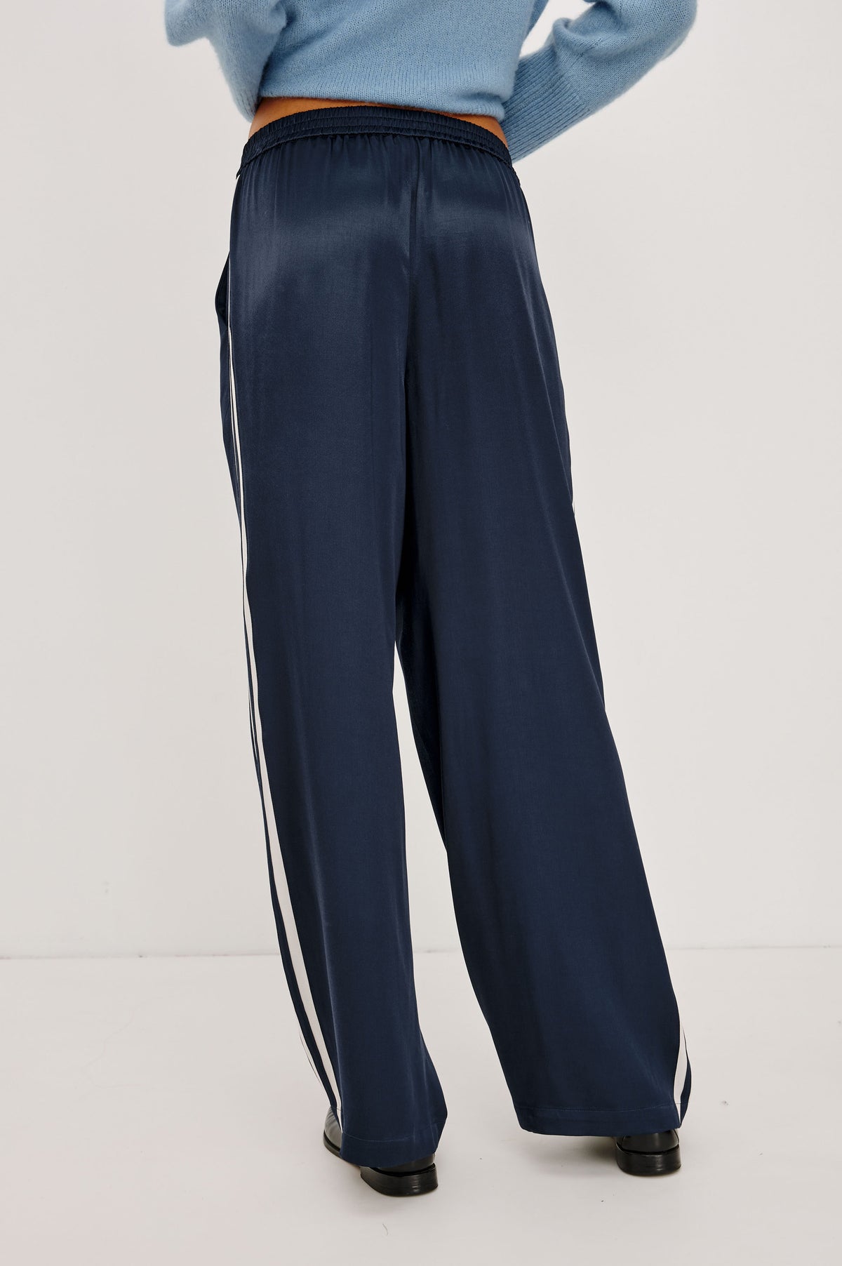 Merida Track Pant in Satin-Back Crepe With Elastic Waist, Side Slant Pockets, Wide Legs, and Contrast Side Stripes in Navy Colorway - Bakc Crop View Featured on Model.