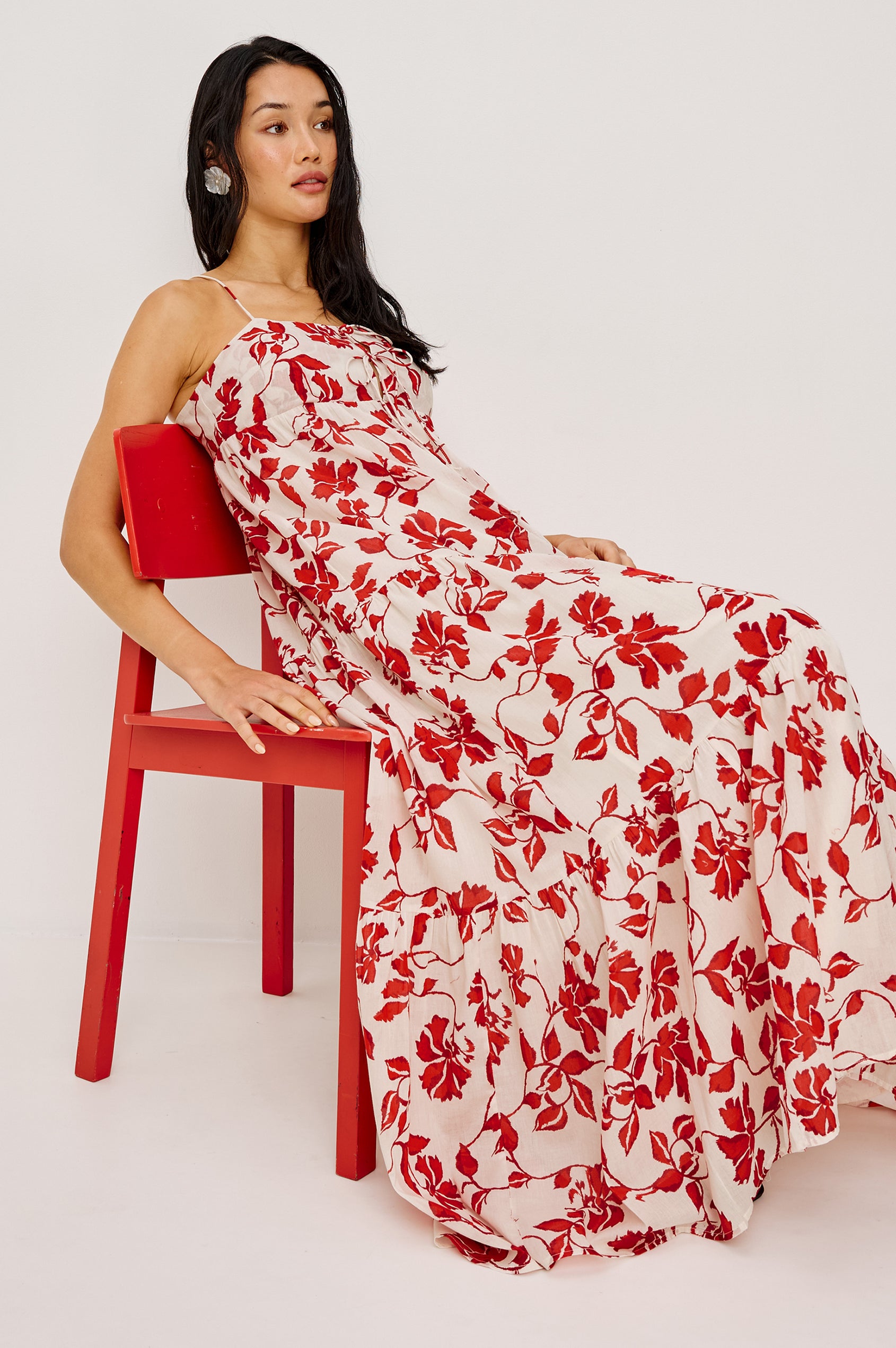 Mica Maxi Dress in Cotton With Adjustable Shoulder Straps Center-Bust Cutout With Adjustable Ties Smocked Back and Fully Lined Tiered Skirt in Red Jasmine Colorway - Full Body Side View Featured on Model Sitting