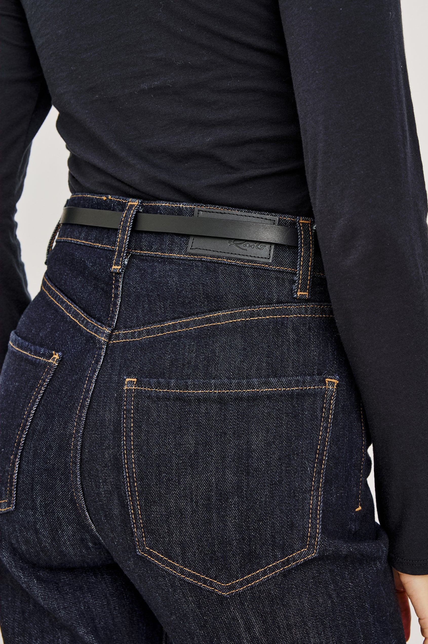 Remi Slim Leather Belt With Adjustable Buckle Closure in Black Gold Colorway - Close Up Back Mid Body View Featured on Model