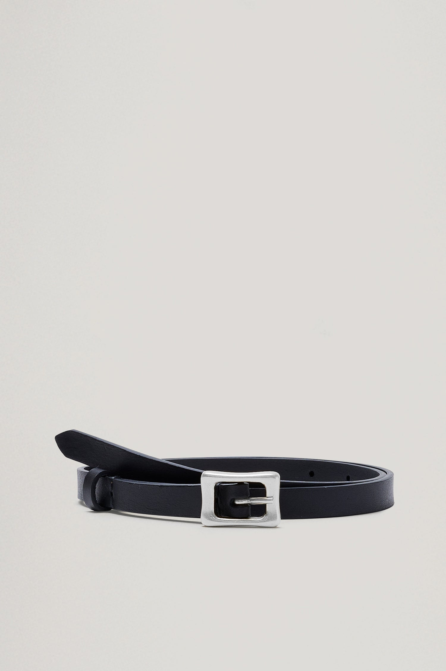 The Remi Belt in Black Leather with a polished silver buckle, buckled and wrapped loosely, front shot.