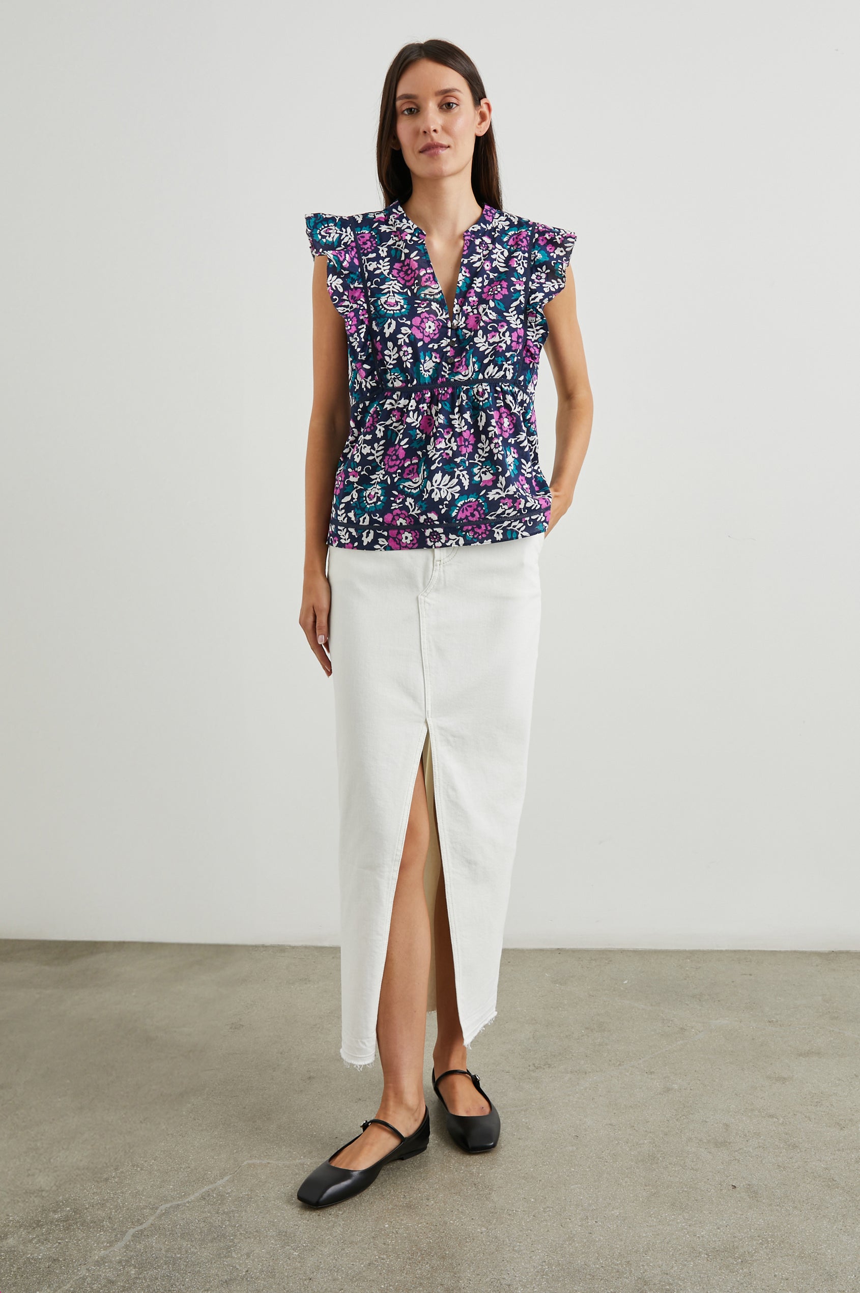 Misha Short Sleeve Top with Flutter Sleeves, a Deep V Neck, and Vertical and Horizontal Black Seams in Woodblock Floral Colorway, Pink, White and Green on Navy - Front Full Body View Featured on Model 