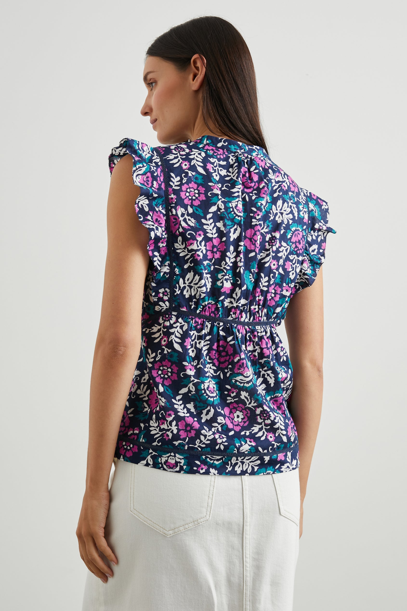Misha Short Sleeve Top with Flutter Sleeves, a Deep V Neck, and Vertical and Horizontal Black Seams in Woodblock Floral Colorway, Pink, White and Green on Navy - Back View Featured on Model 