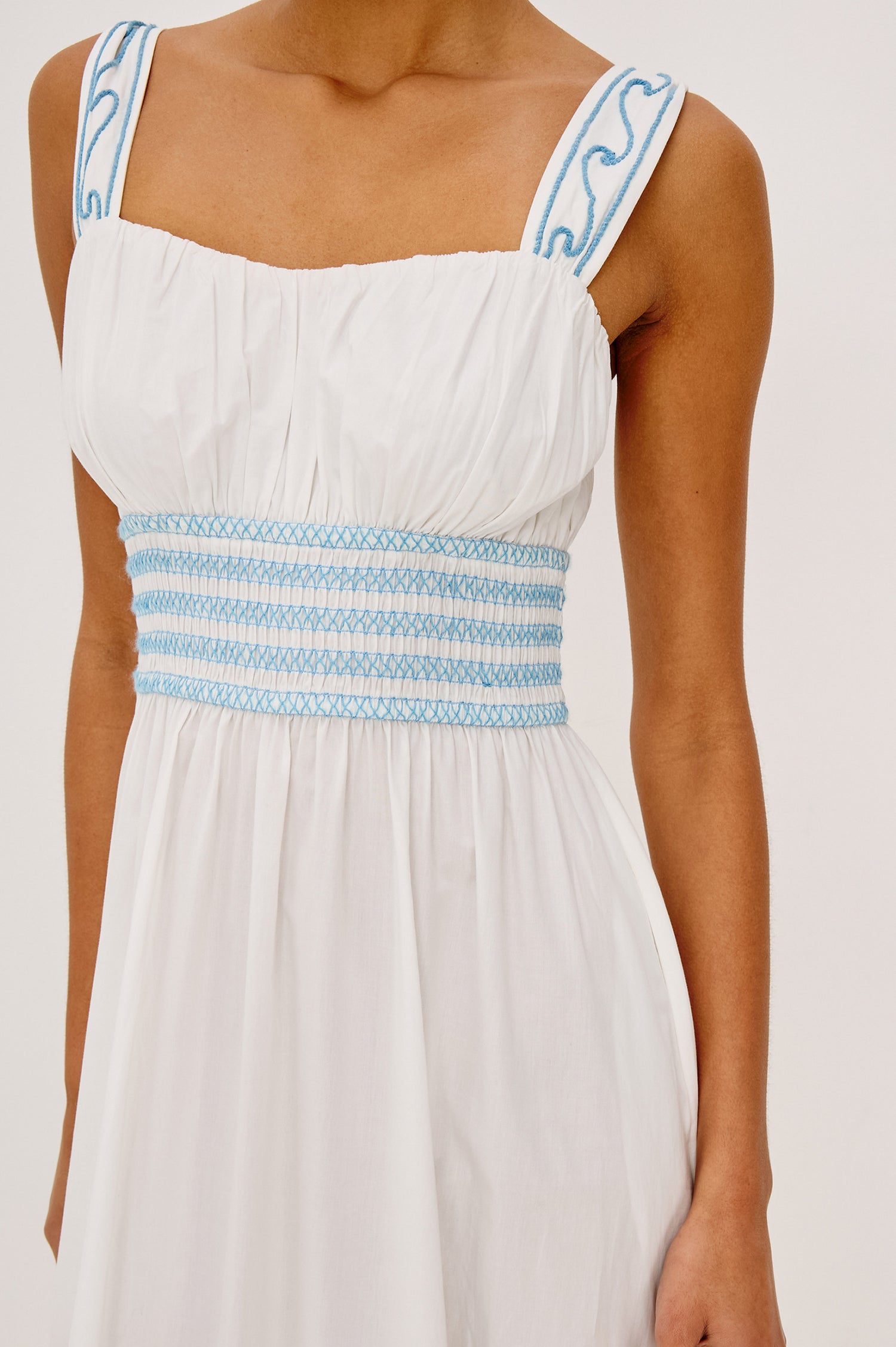 Moira Midi Dress in Cotton Poplin With Wide Embroidered Shoulder Straps Soft Sweetheart Neckline Smocked Empire Waist Fully Lined Skirt With Floral Cutwork at Hem in a White Colorway With Blue Embroidery Details - Upper Body Front View Zoomed In Details Featured on Model