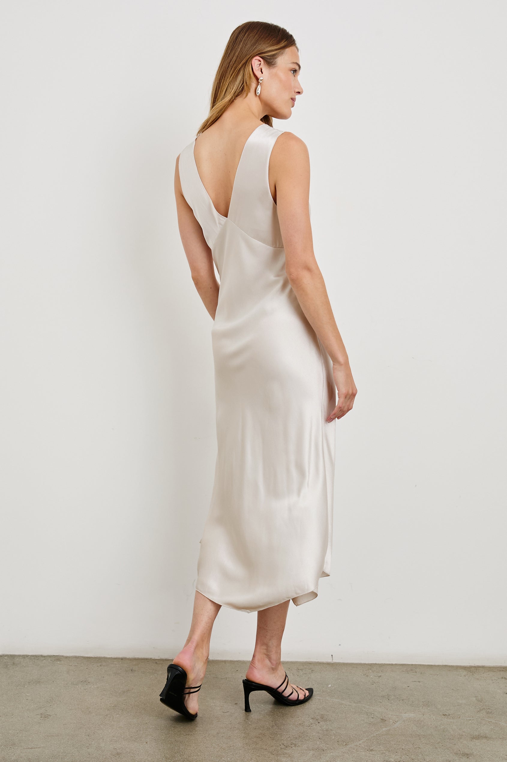 Monique Sleeveless Midi Dress with an Asymmetrical Hem Line, Side Slit, Deep V Neck, and Wide Shoulder Straps in Ivory Colorway - Back Full Body View Featured on Model