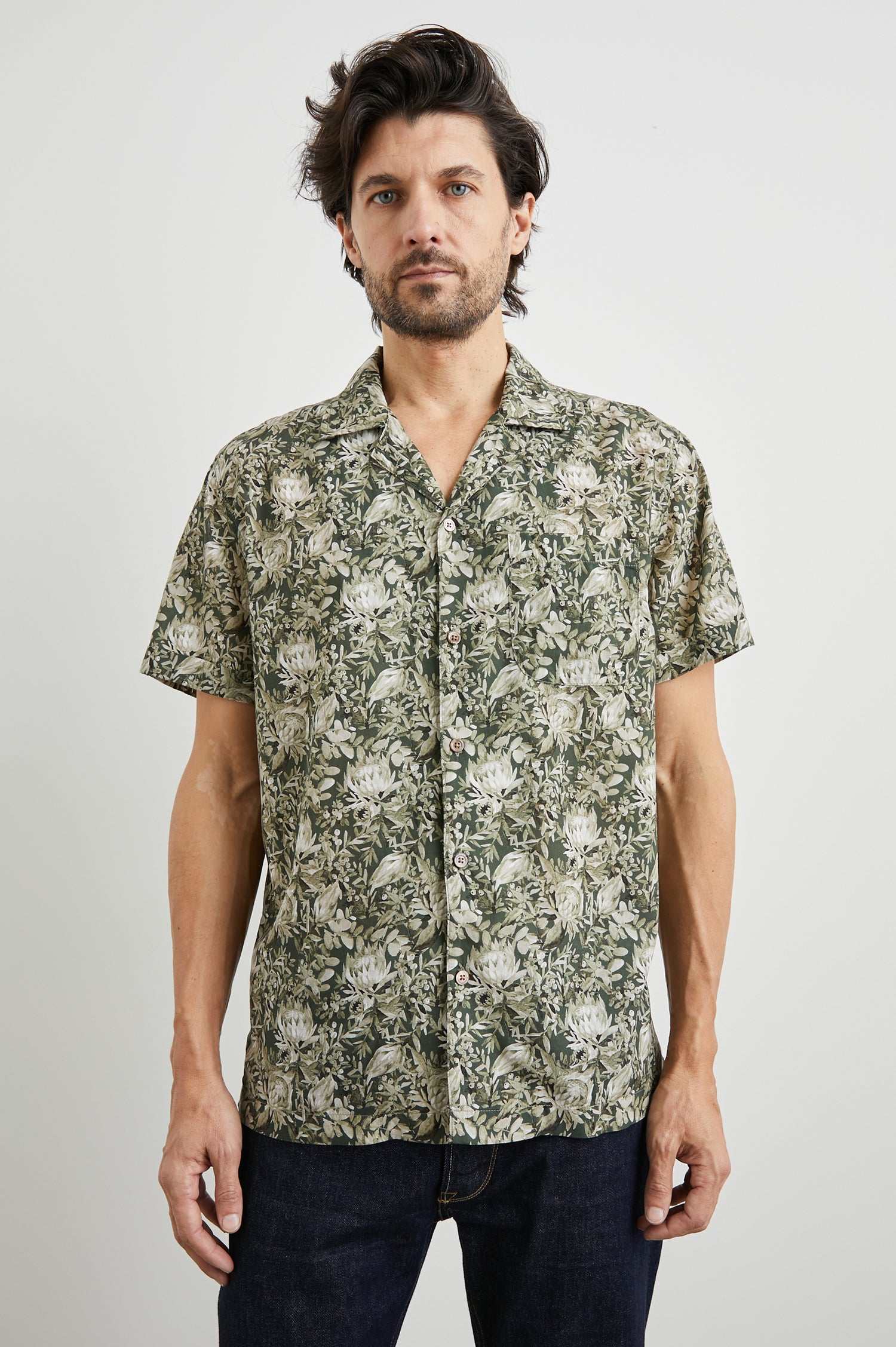 Moreno Short Sleeve Button Up with a Chest Patch Pocket in Watercolor Olive Brass Colorway, a Floral Print in Greens and White  - Front View Featured on Model