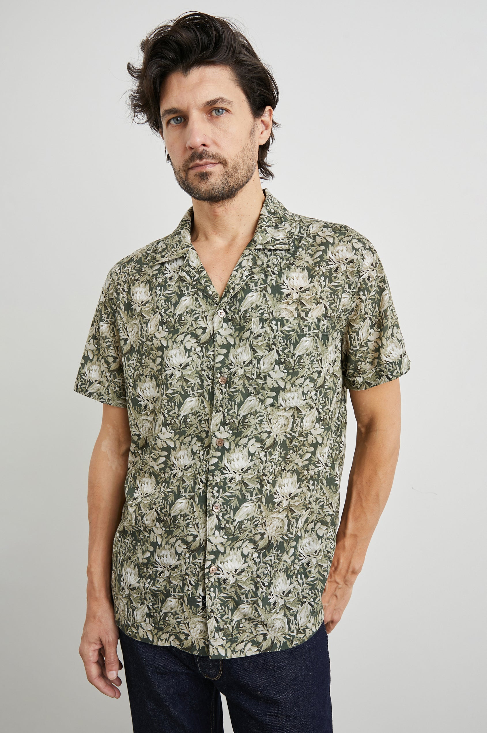 Moreno Short Sleeve Button Up with a Chest Patch Pocket in Watercolor Olive Brass Colorway, a Floral Print in Greens and White  - Front View Featured on Model