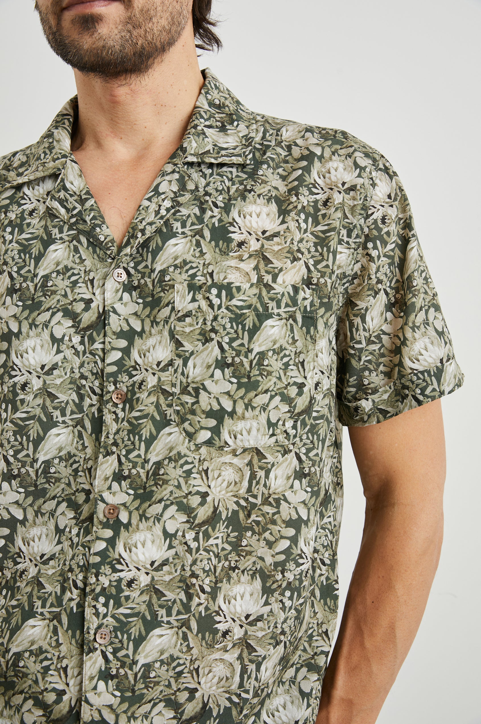 Moreno Short Sleeve Button Up with a Chest Patch Pocket in Watercolor Olive Brass Colorway, a Floral Print in Greens and White  - Front View Featured on Model