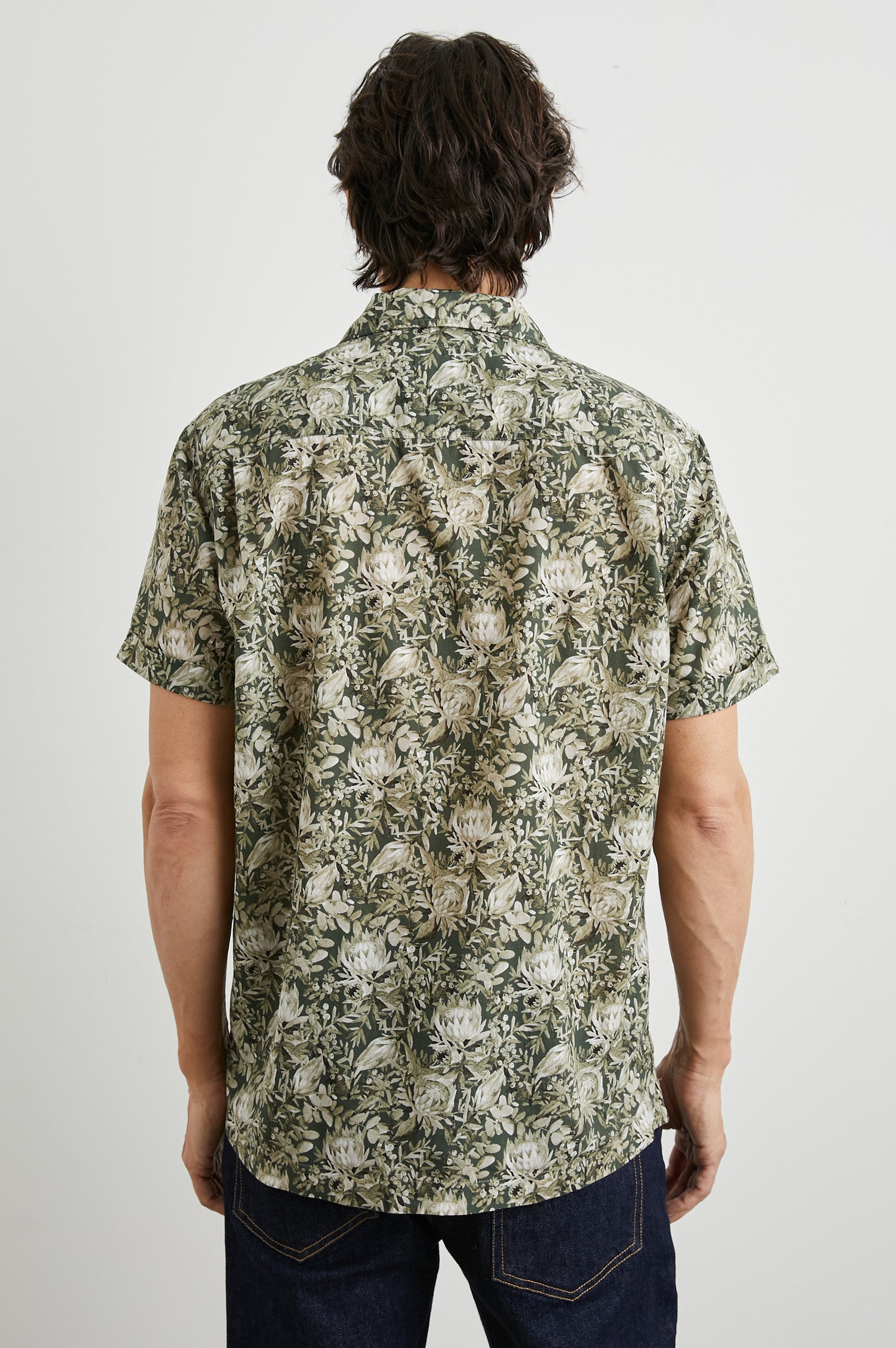 Moreno Short Sleeve Button Up with a Chest Patch Pocket in Watercolor Olive Brass Colorway, a Floral Print in Greens and White  - Back View Featured on Model