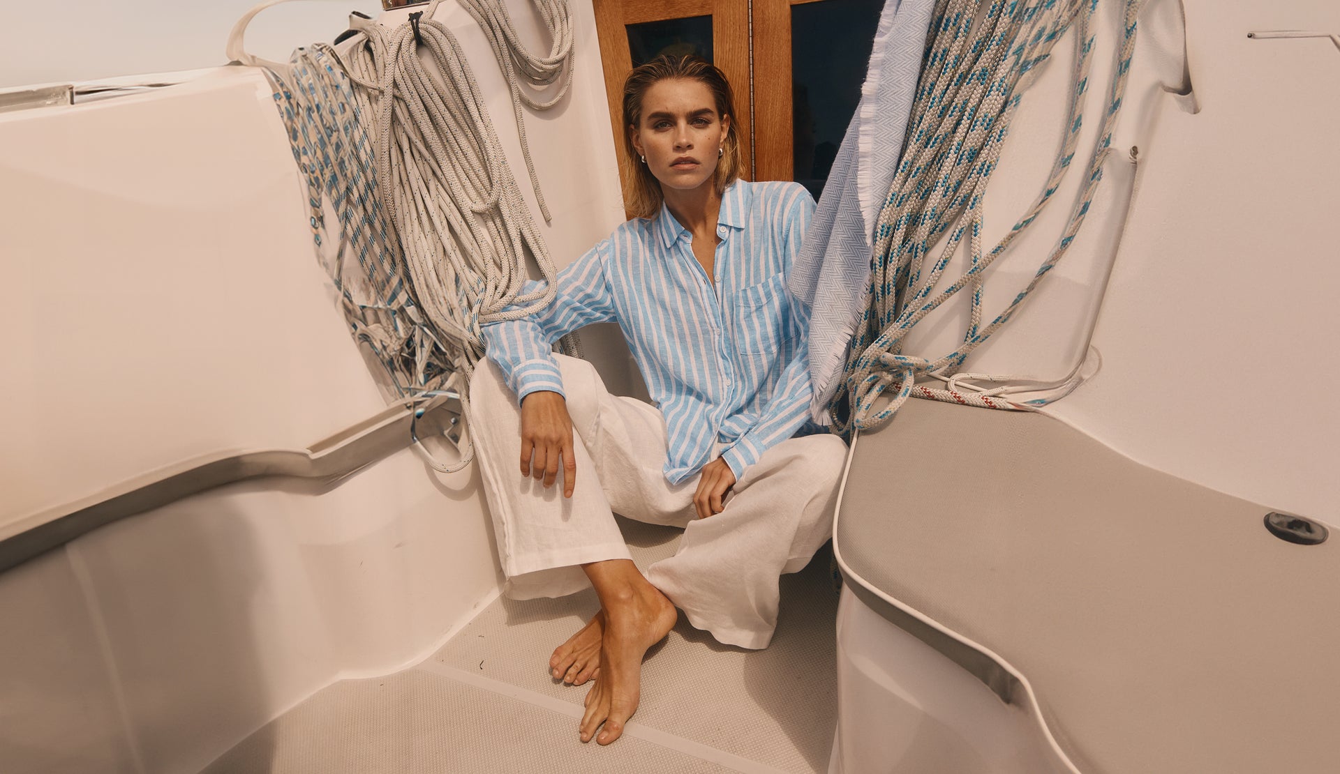 EDITORIAL IMAGE OF MODEL SITTING ON A BOAT WEARING CHARLI SHIRT