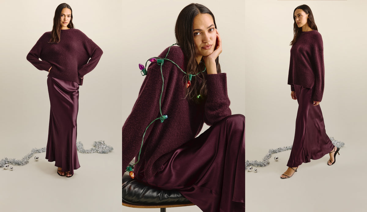 A woman modeling a matching burgundy knit sweater and satin maxi skirt set against a light beige studio background with silver tinsel on the floor.
