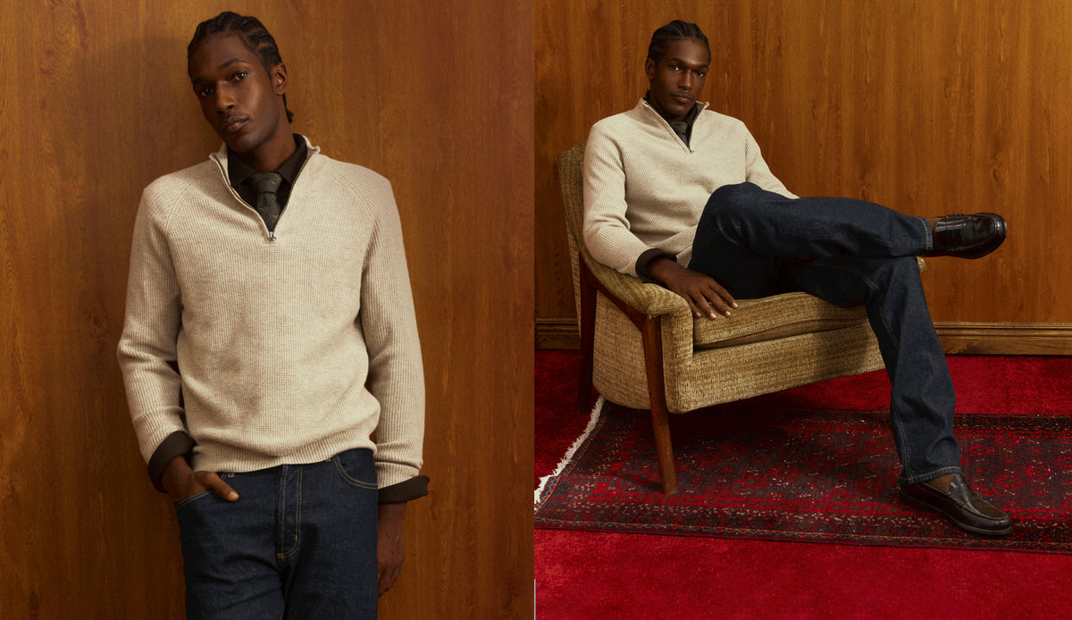 A split-screen lifestyle photo of a male model wearing a cream-colored quarter-zip sweater and dark blue jeans, posed against a wood-paneled wall and sitting in a woven armchair on a red patterned rug.