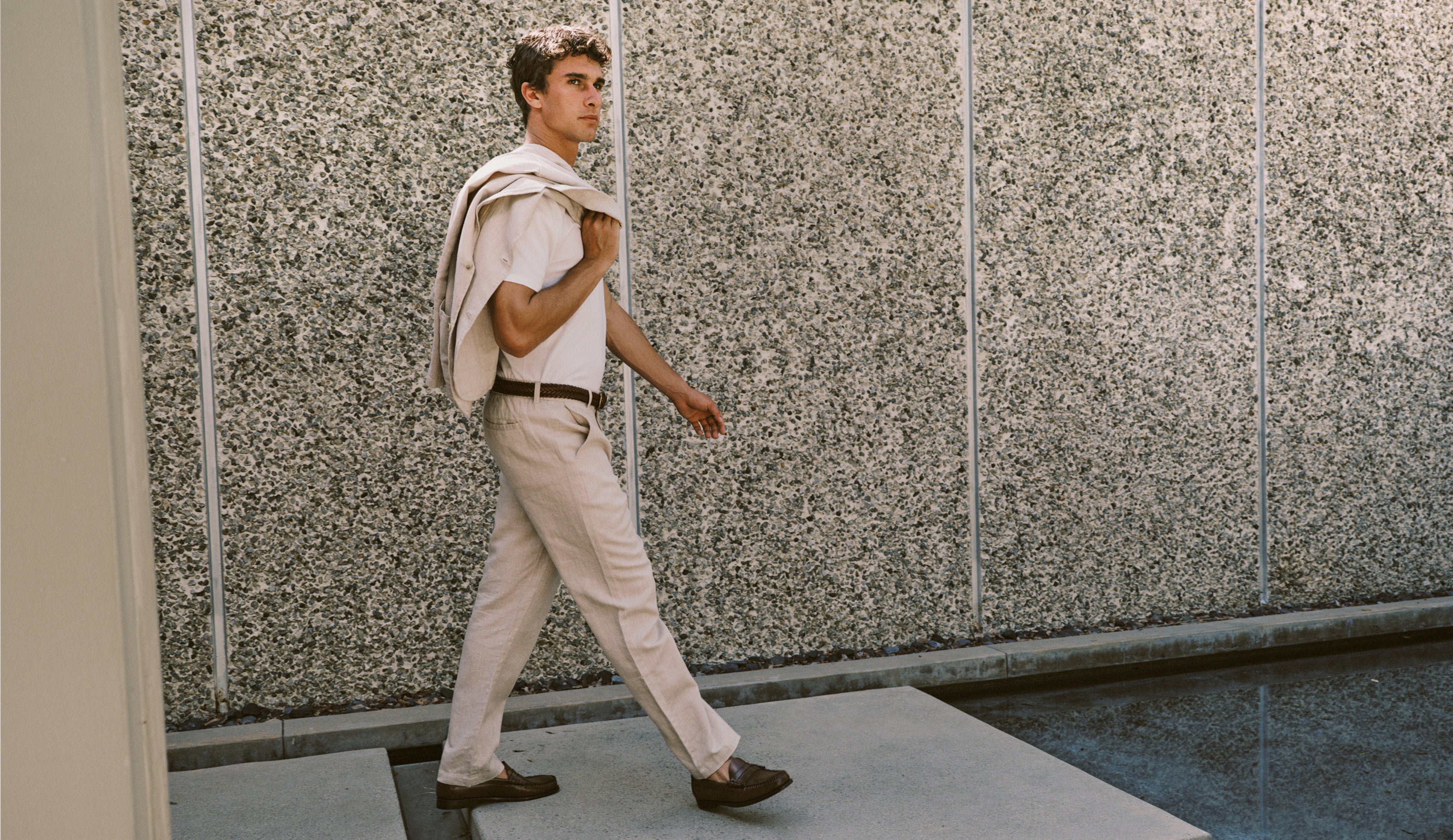 Man wearing a beige suit walking near a pool