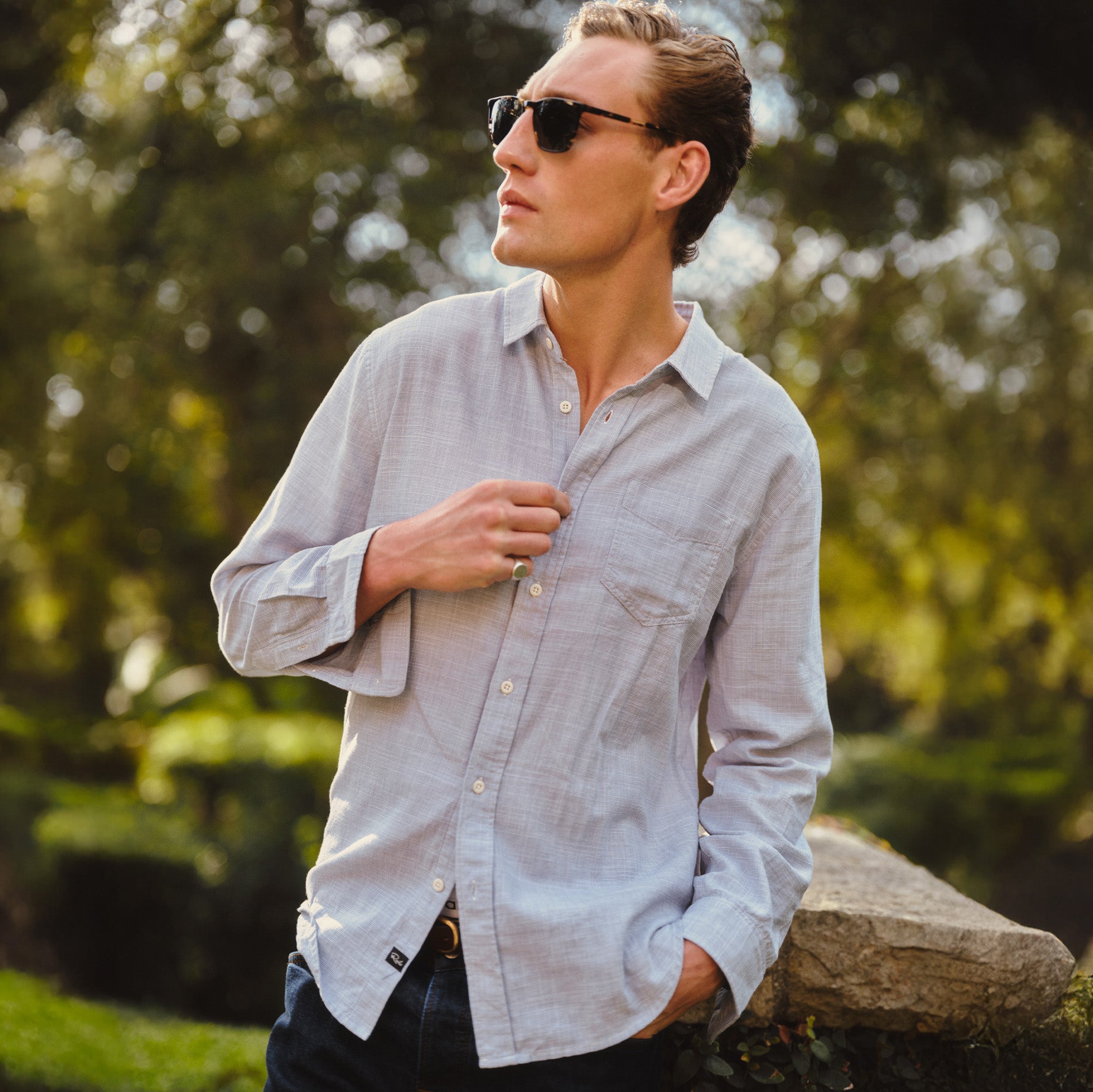 Man in a light blue button down shirt while looking away in a garden setting