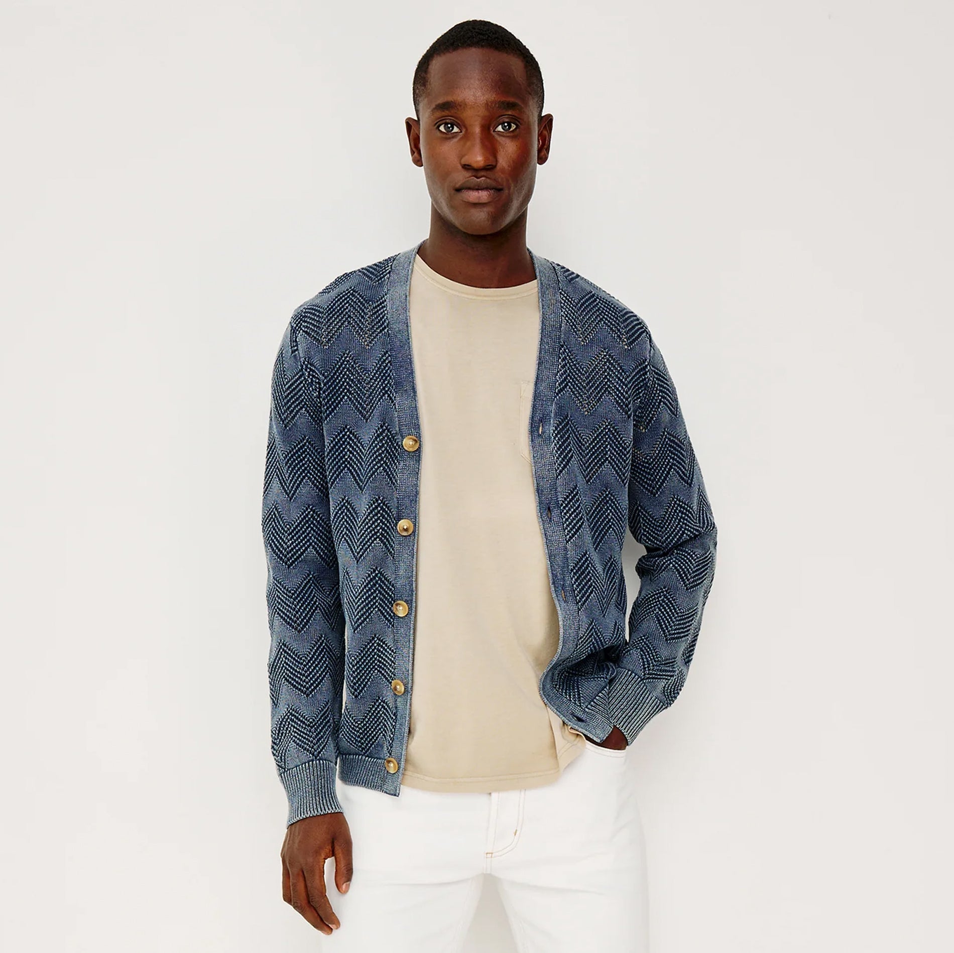 Man wearing a blue patterned cardigan over a beige shirt on a white background